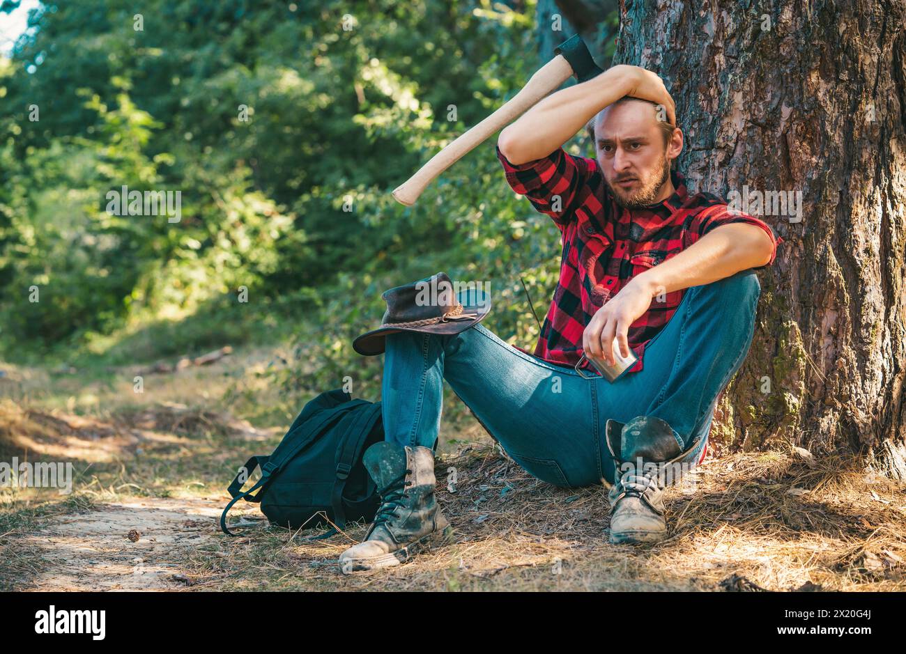 Homme bûcheron assis dans la forêt. L'exploitation forestière illégale se poursuit aujourd'hui. Ouvrier bûcheron debout dans la forêt avec une hache. Agriculture et sylviculture Banque D'Images