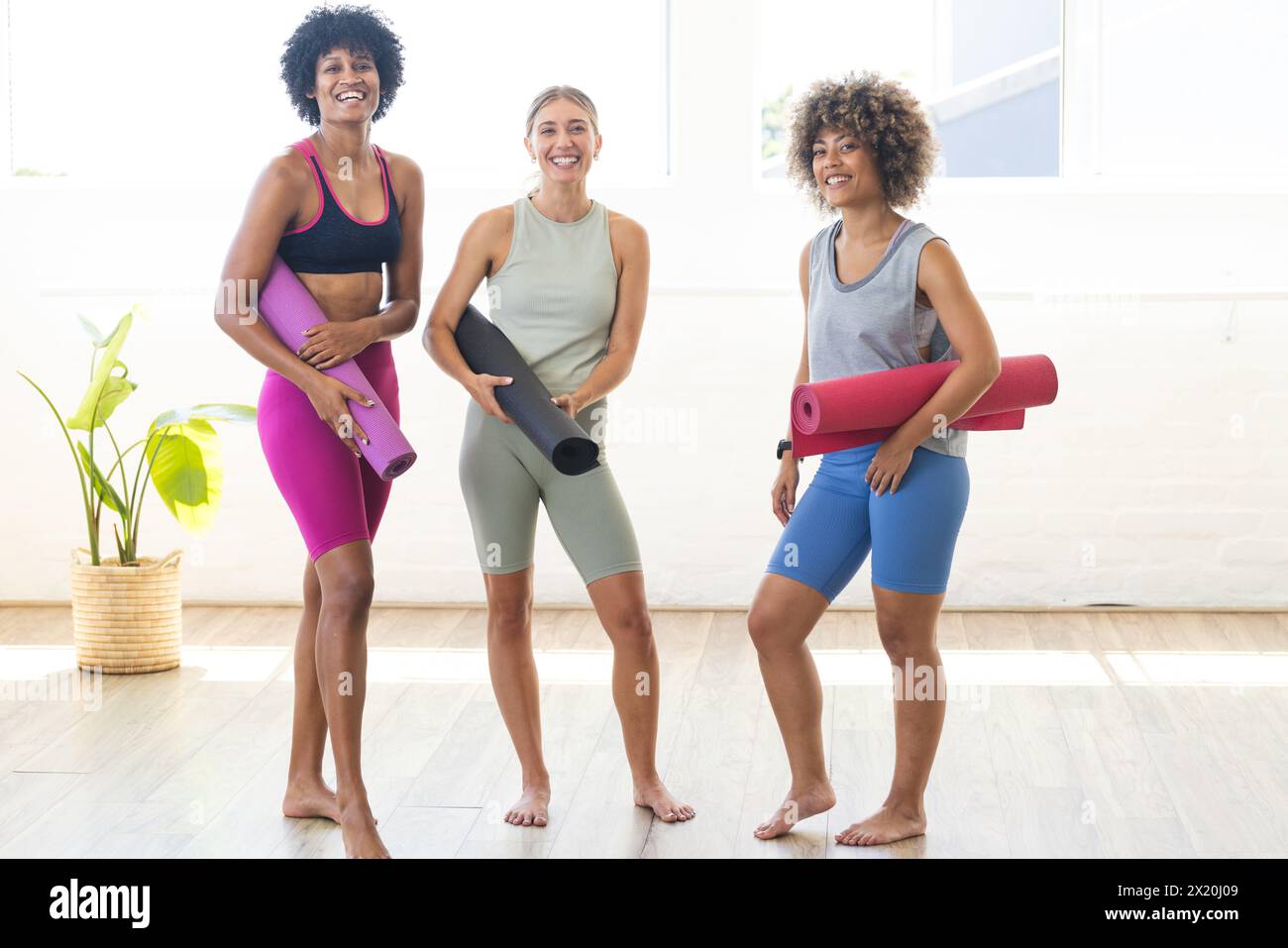 Trois femmes diverses tiennent des tapis de yoga, debout ensemble, souriantes Banque D'Images