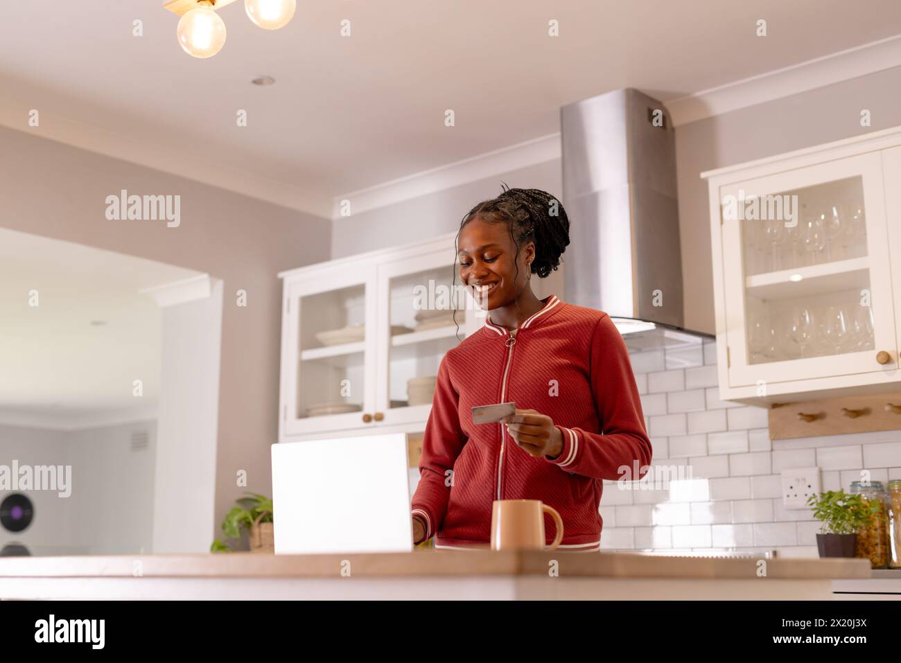 Jeune femme noire avec des cartes de crédit, debout dans la cuisine près d'un ordinateur portable ouvert Banque D'Images