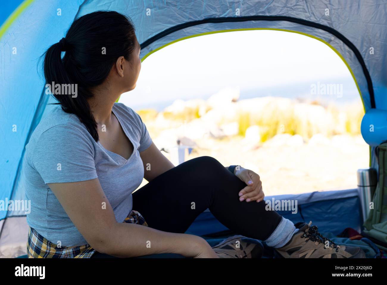Randonneur féminin biracial assis à l'intérieur de la tente, regardant dehors à la nature de l'aventure. Elle a les cheveux foncés, la peau brun clair, et porte des randonnées occasionnelles Banque D'Images