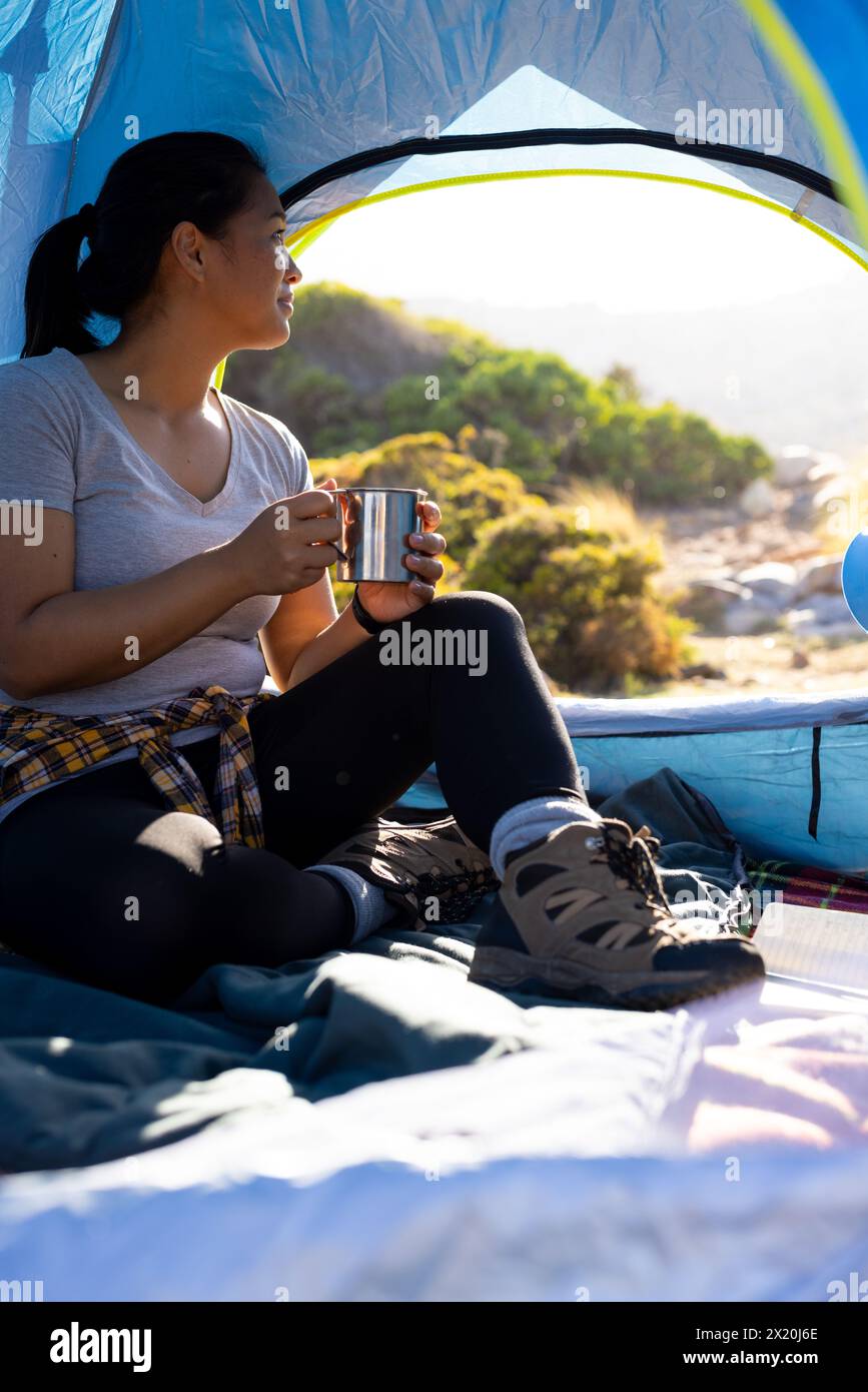 Randonneur féminin biracial avec les cheveux foncés appréciant le café à l'intérieur de la tente Banque D'Images