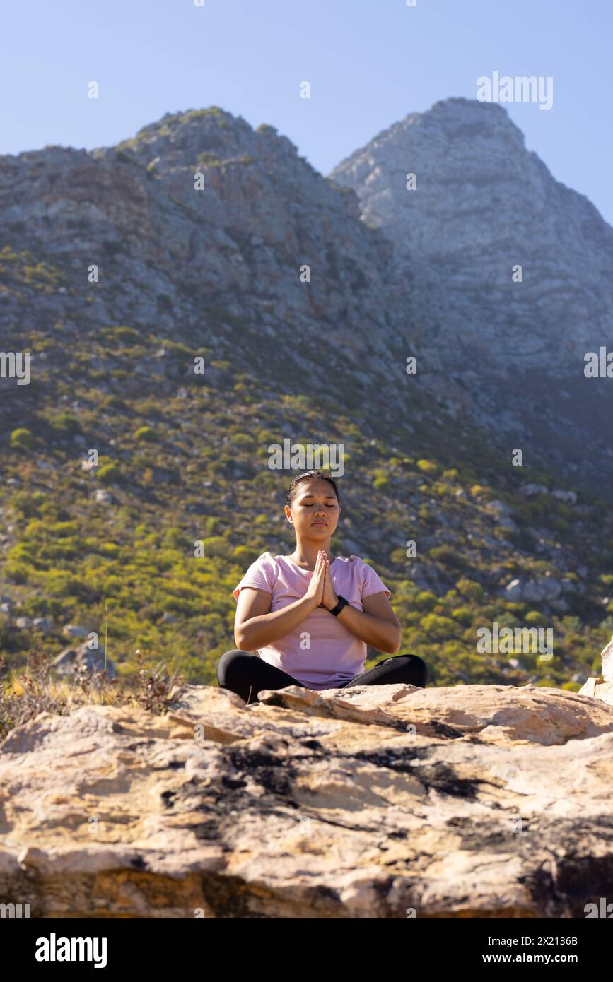 Randonneur féminin biracial appréciant le yoga dans les montagnes, les mains en position de prière. Elle a les cheveux foncés, portant des vêtements de sport décontractés, l'air paisible, inaltérée, Banque D'Images