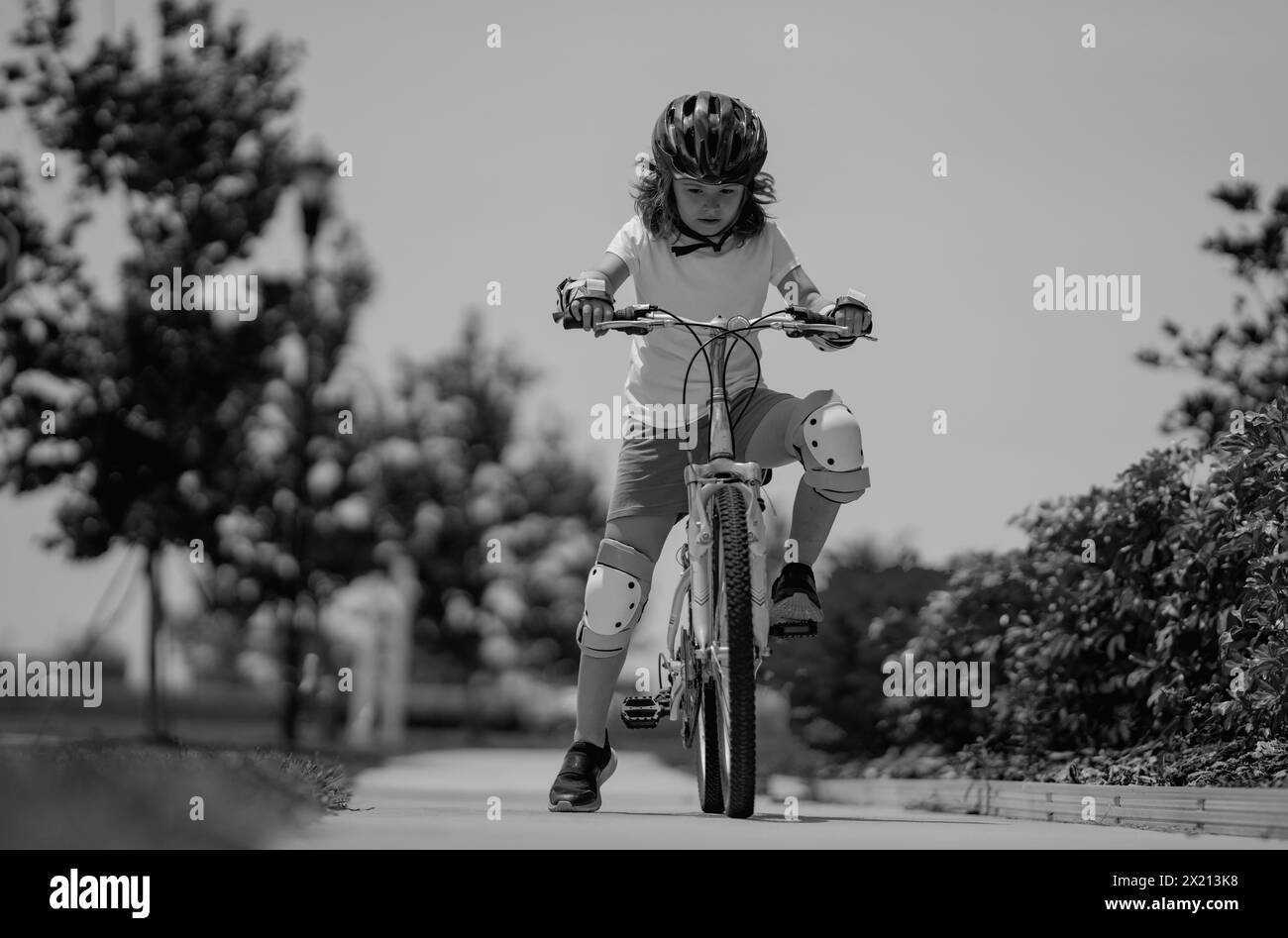 Un petit enfant qui fait du vélo dans le parc d'été. Les enfants apprennent à conduire un vélo sur une allée à l'extérieur. Enfant à vélo dans la ville portant des casques comme Banque D'Images