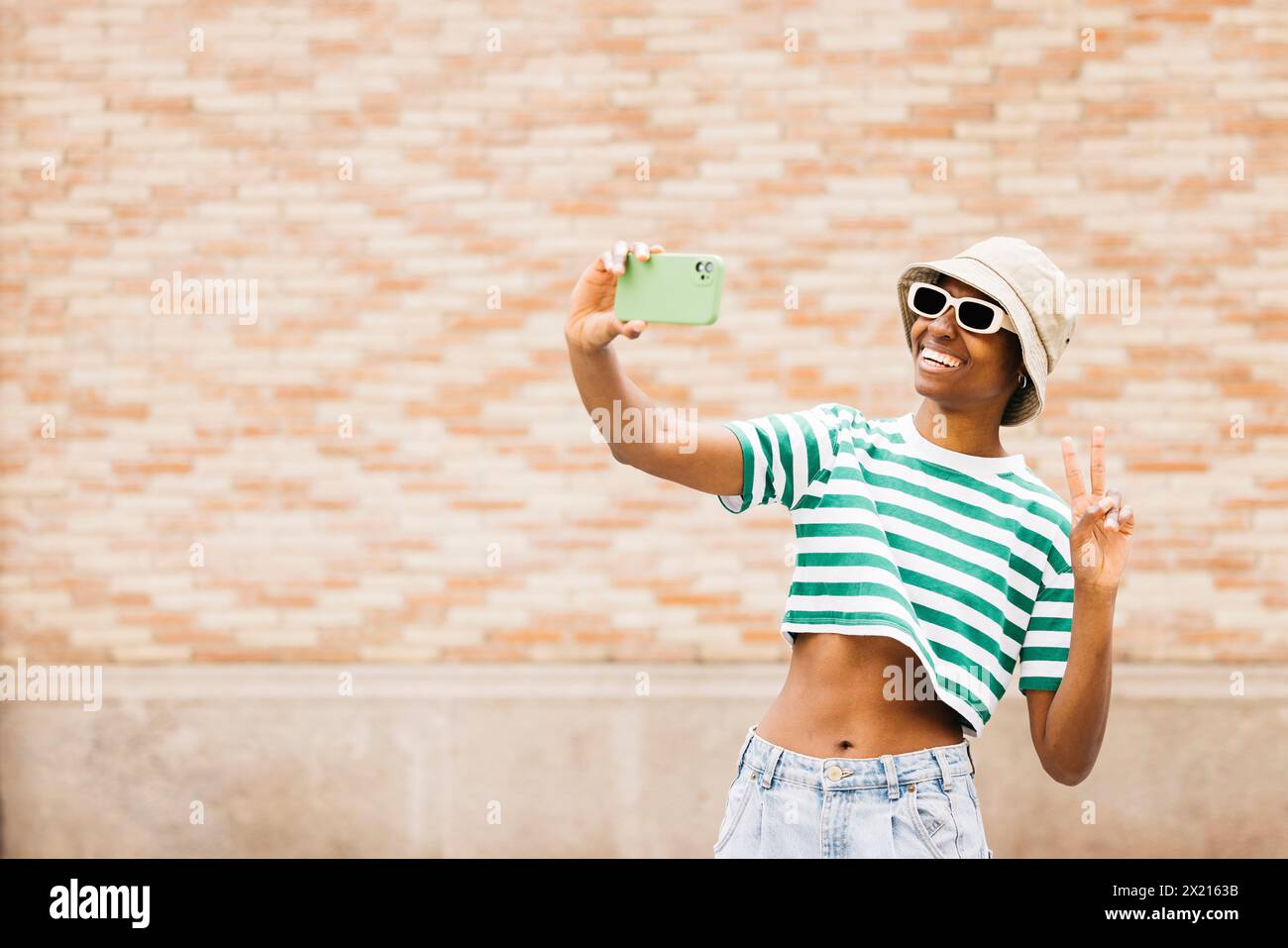 Portrait en plein air d'une jeune femme joyeuse portant des lunettes de soleil et un chapeau et prenant un selfie. Jeune femme souriant joyeusement dans un cadre extérieur. Banque D'Images