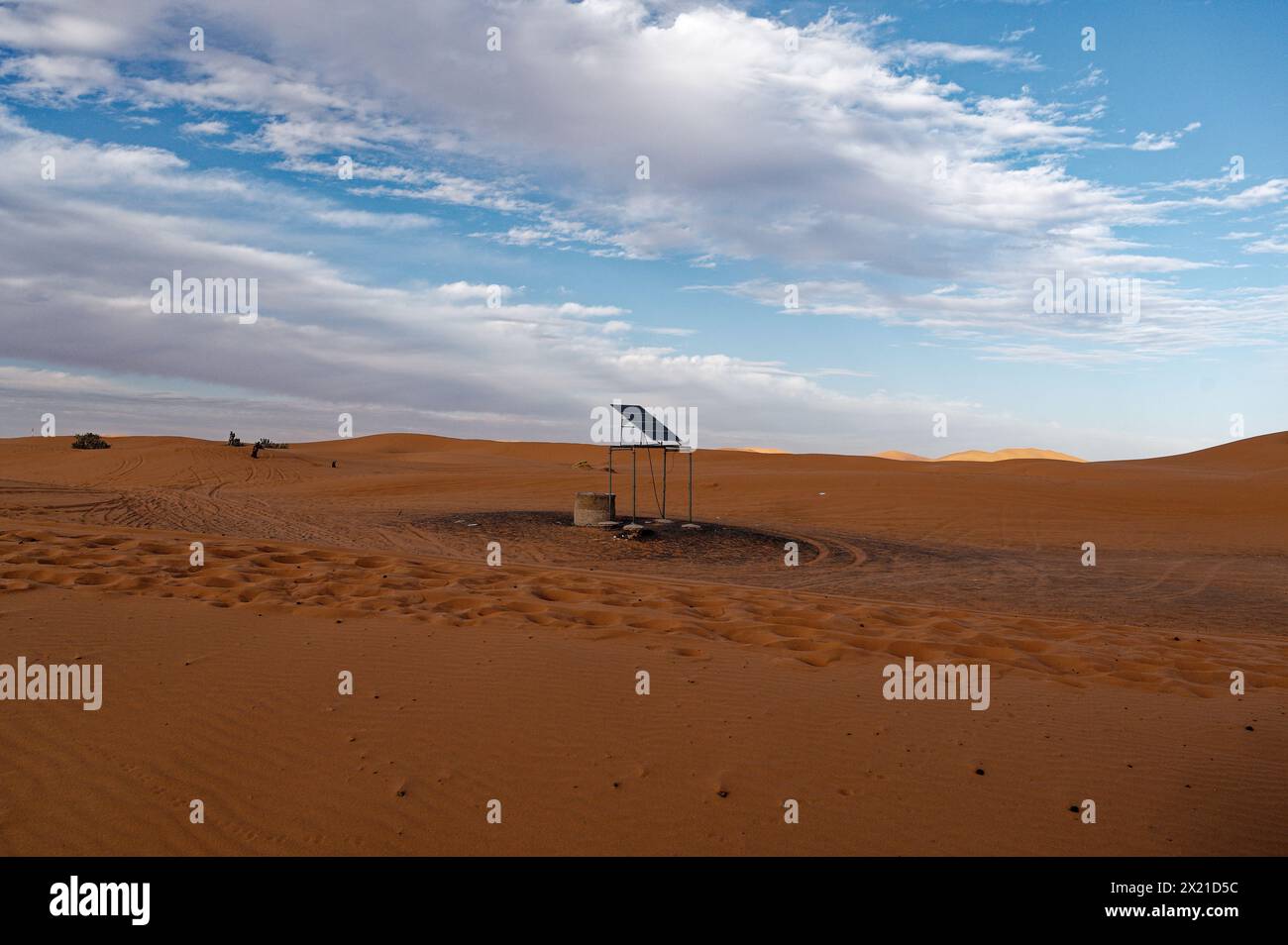 Un panneau solaire solitaire, perché sur un mince cadre métallique au-dessus des sables du désert de Merzouga, avec des pistes de véhicules tissant un motif circulaire en dessous. Banque D'Images