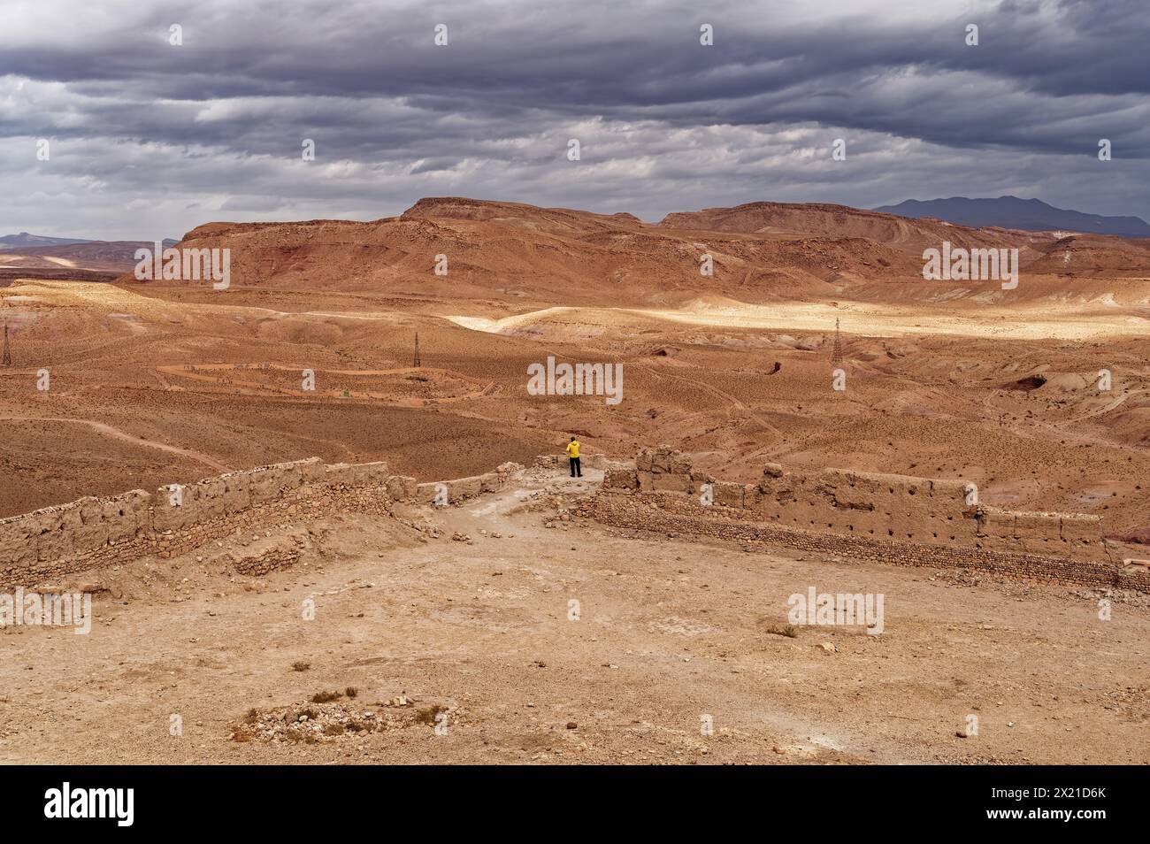 Au sommet d'Aït Benhaddou, une figure solitaire contraste l'immense étendue désertique sous un ciel couvert. Banque D'Images