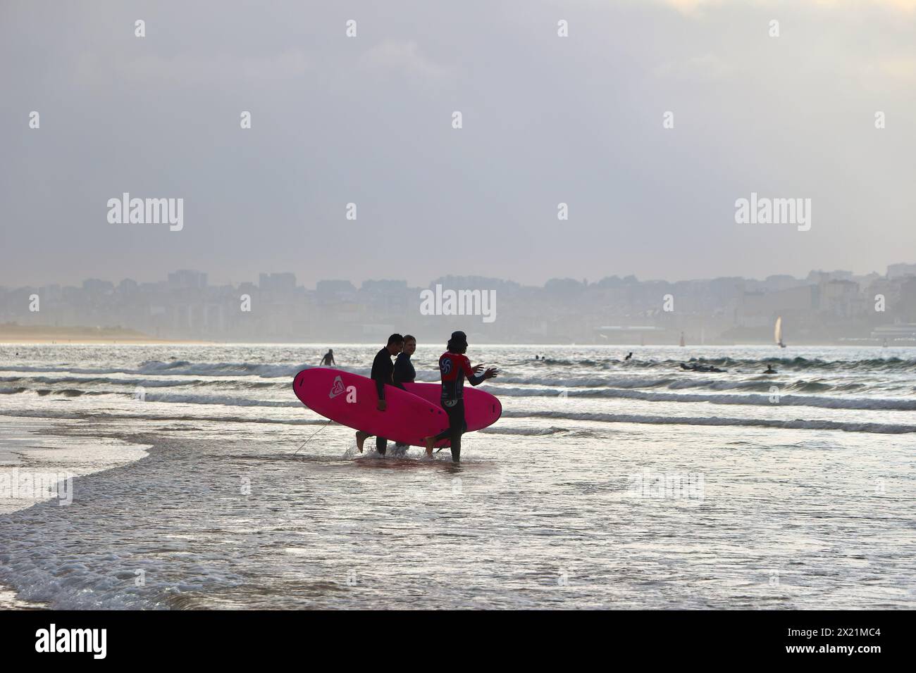 Vue sur la baie de Santander avec des surfeurs dans le surf peu profond portant des planches de surf au cours d'une leçon en fin d'après-midi Ribamontán al Mar Cantabria Espagne Banque D'Images