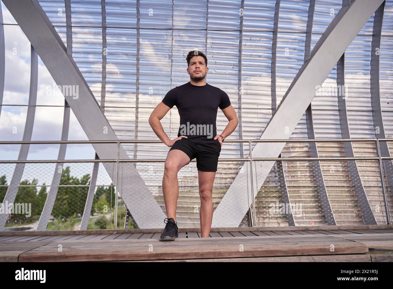 homme latin en sportswear posant avec une jambe sur un banc et les mains dans les poches Banque D'Images