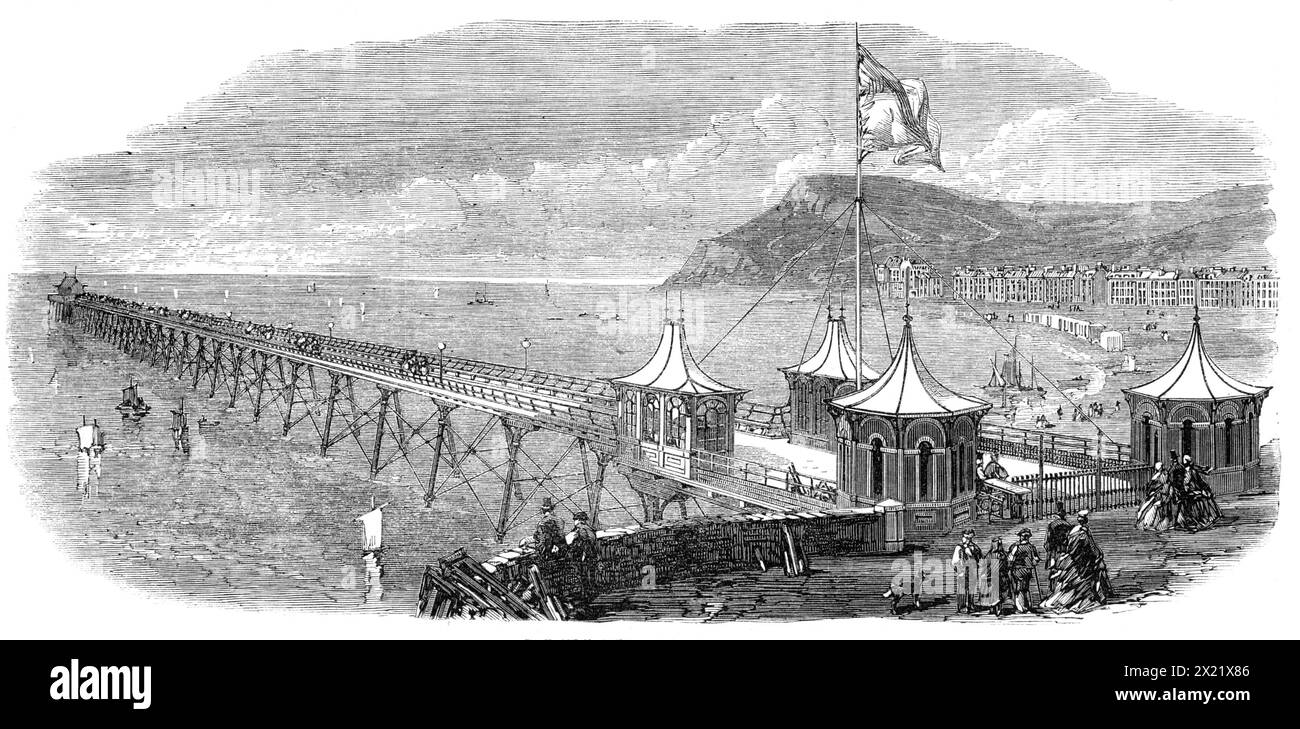 La nouvelle jetée à Aberystwith, [pays de Galles], 1865. Cette jetée a été construite à partir des plans de Mr. Birch C.E.,... l'entrepreneur étant Mr. Dawson. Il est de 800 pieds. en longueur, par 20 pieds. large, sauf à l'entrée et à la tête, qui sont de 120 pieds. en largeur, afin de permettre l'espace pour les bazars de fantaisie et un salon de rafraîchissement. Sur toute la longueur de la promenade des sièges sont construits, capables d'accueillir 2000 personnes, tandis que des lampes belles et durables, au nombre de seize, sont érigées à de courts intervalles, donnant un effet joyeux et gracieux à l'ensemble. La jetée est supportée sur de la fonte Banque D'Images