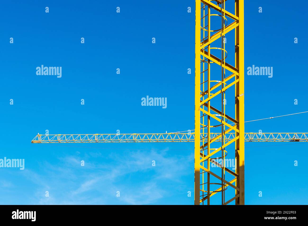 Deux grues de construction jaunes formant une croix comme fond abstrait contre le ciel bleu Banque D'Images