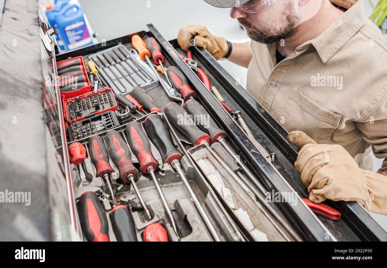 Mécanicien automobile caucasien à la recherche d'un outil droit dans un grand tiroir à boîte à outils Banque D'Images