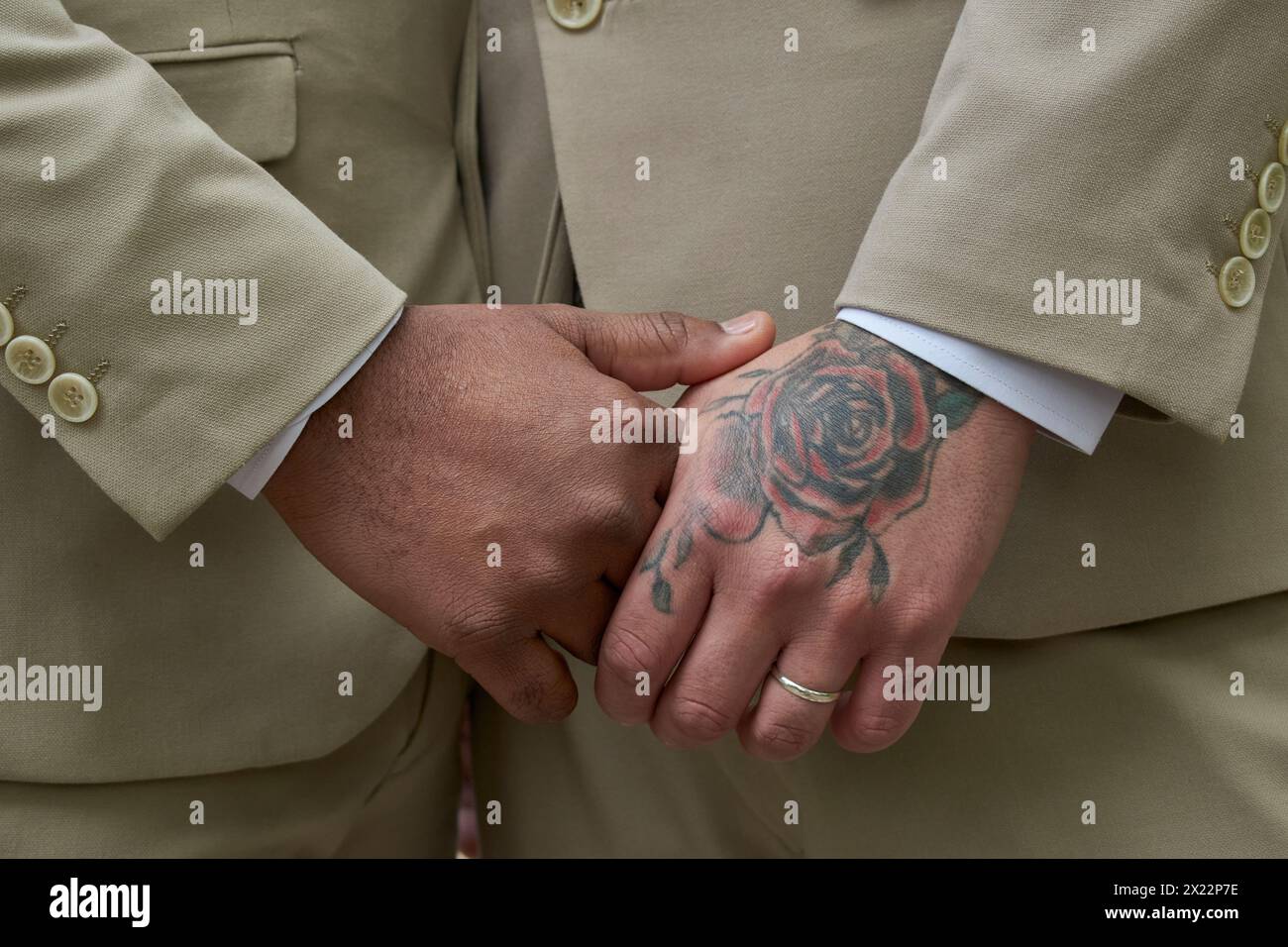 Deux hommes en costumes se tenant la main et un a un tatouage rose sur sa main. Concept d'amour et d'unité entre les deux hommes Banque D'Images