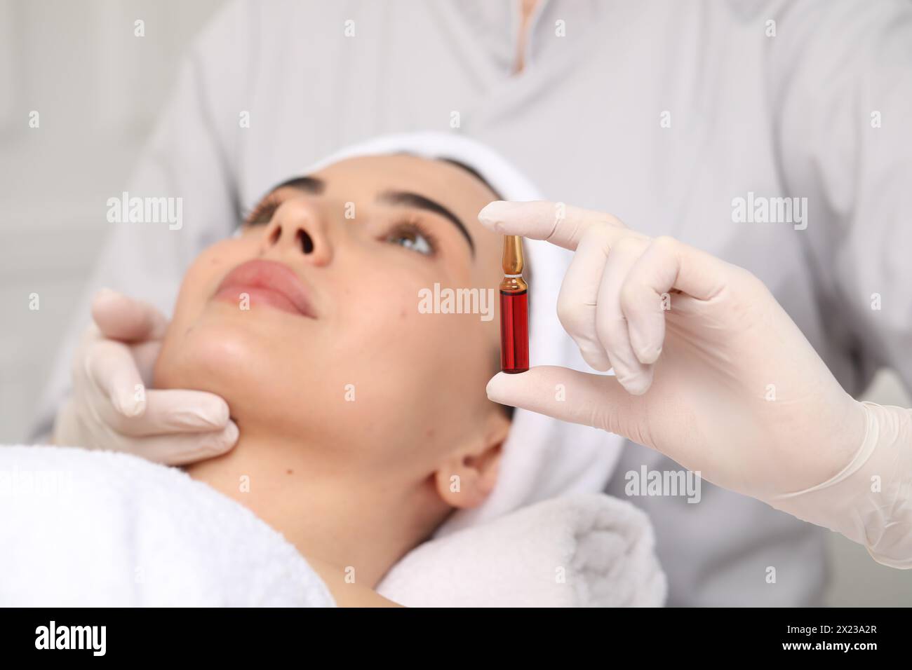 Cosmétologue professionnel tenant l'ampoule de soins de la peau tout en travaillant avec le client en clinique, gros plan Banque D'Images