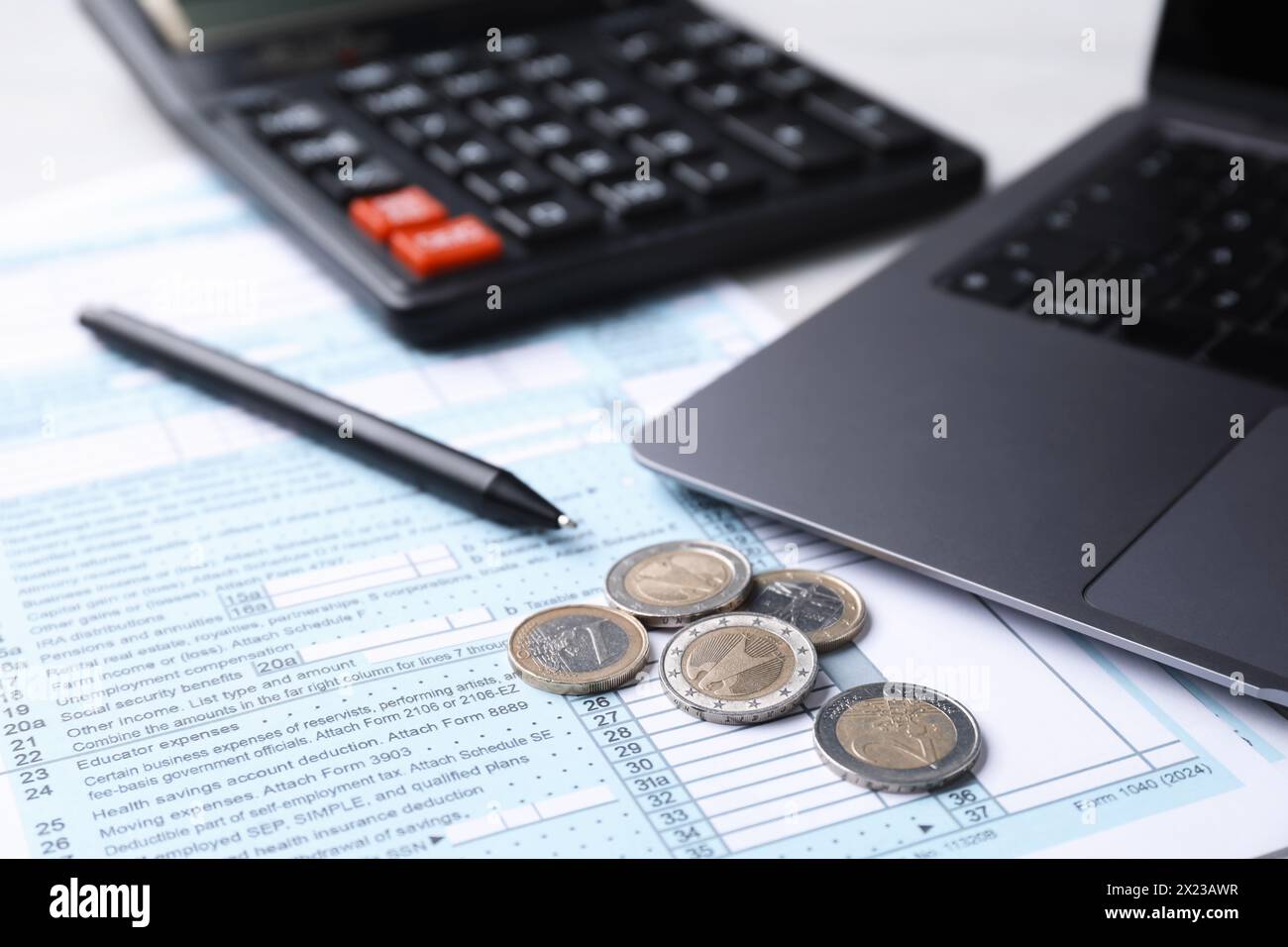 Formulaires fiscaux, pièces de monnaie, stylo, calculatrice et ordinateur portable sur la table, gros plan Banque D'Images
