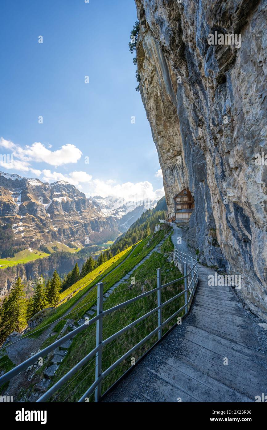 Description : cabane suisse en bois Gasthaus Aescher-Wildkirchli en dessous d'un mur de roche massif surpenchant et montagne pittoresque en arrière-plan. Seealpsee, A Banque D'Images