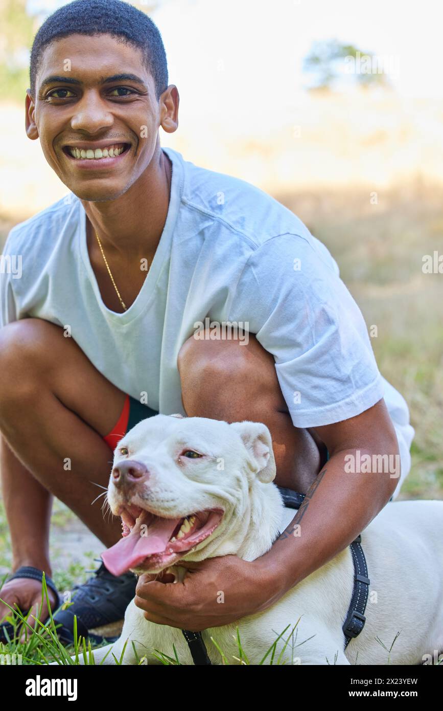 Jeune homme, portrait et chien sur la pelouse avec bonheur, jouant avec pitbull pour l'amour des animaux de compagnie et le plaisir en plein air. Adoption, favoriser et lier dans le parc avec Banque D'Images