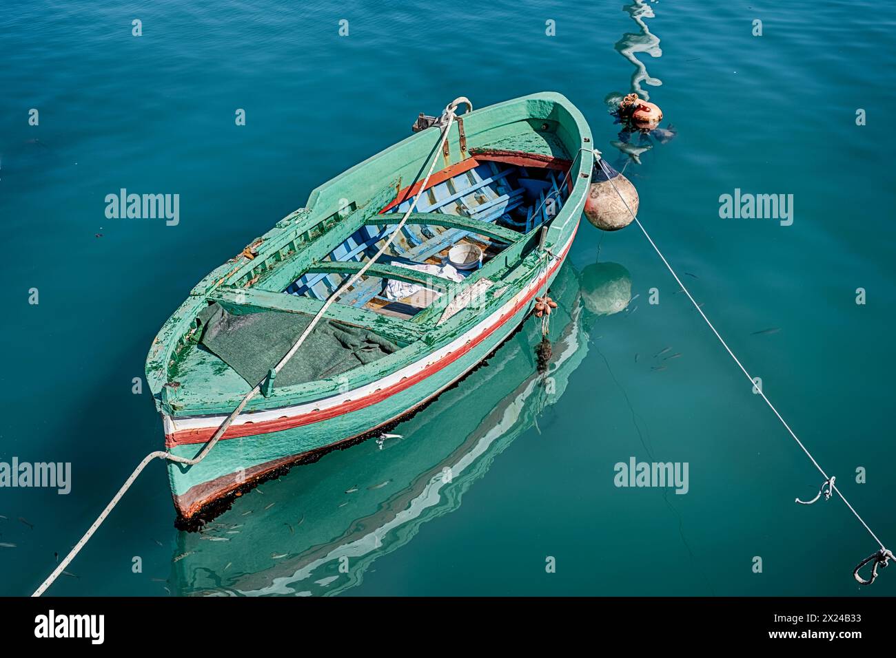 Un bateau en bois vert est amarré dans l'un des petits ports en pierre de la ville de Siricusa, en Italie. Banque D'Images