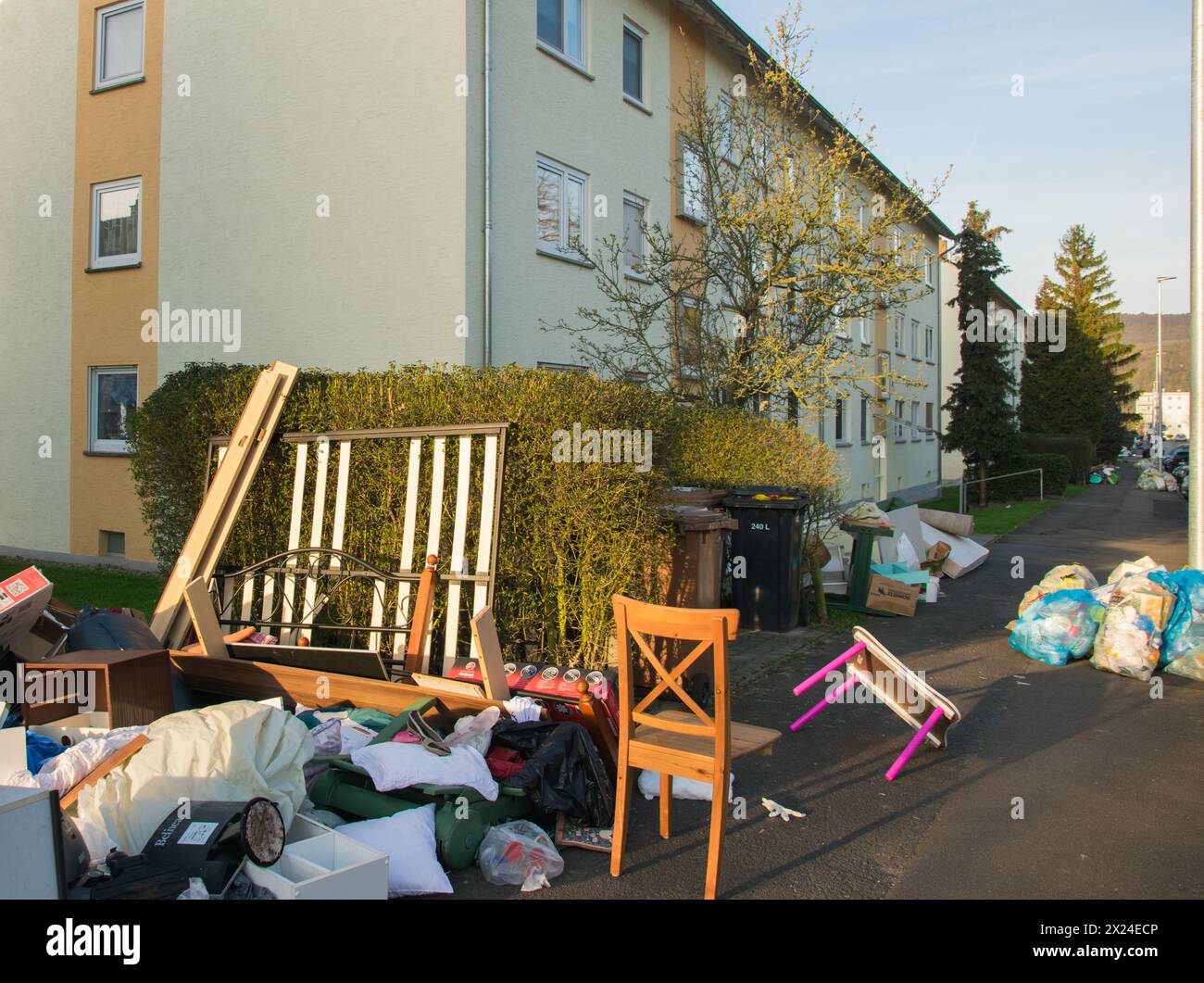 Déchets dans une ville près de la maison. Grandes ordures avec vieux meubles en bois, jouets, boîtes, sacs en plastique dans une rue et l'herbe verte dans la décharge ensoleillée jour après jour Banque D'Images