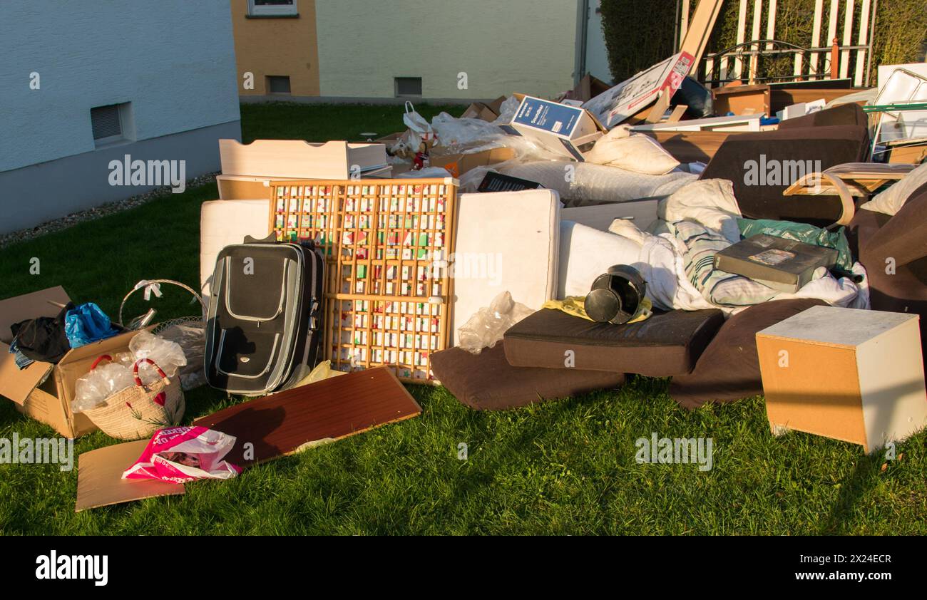 Déchets dans une ville près de la maison. Grandes ordures avec vieux meubles en bois, jouets, boîtes, sacs en plastique dans une rue et l'herbe verte dans la décharge ensoleillée jour après jour Banque D'Images