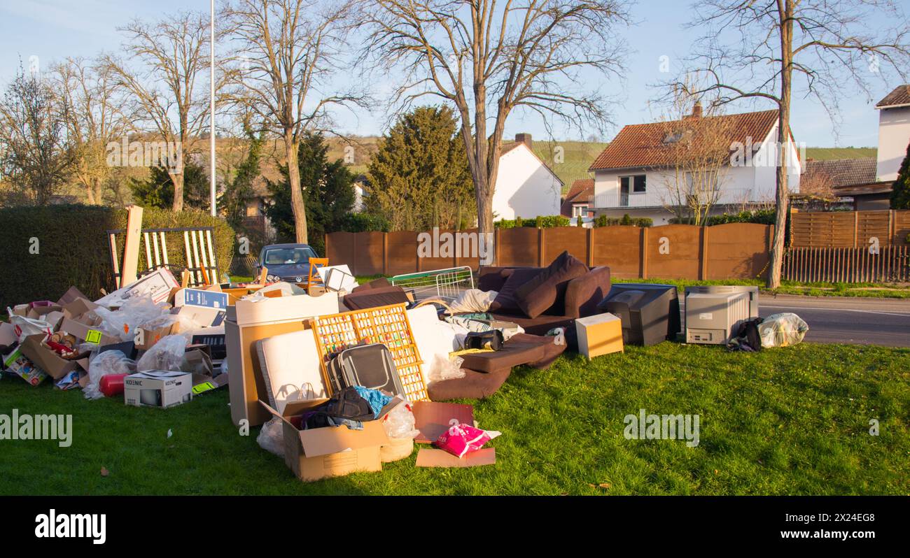 Déchets dans une ville près de la maison. Grandes ordures avec vieux meubles en bois, jouets, boîtes, sacs en plastique dans une rue et l'herbe verte dans la décharge ensoleillée jour après jour Banque D'Images