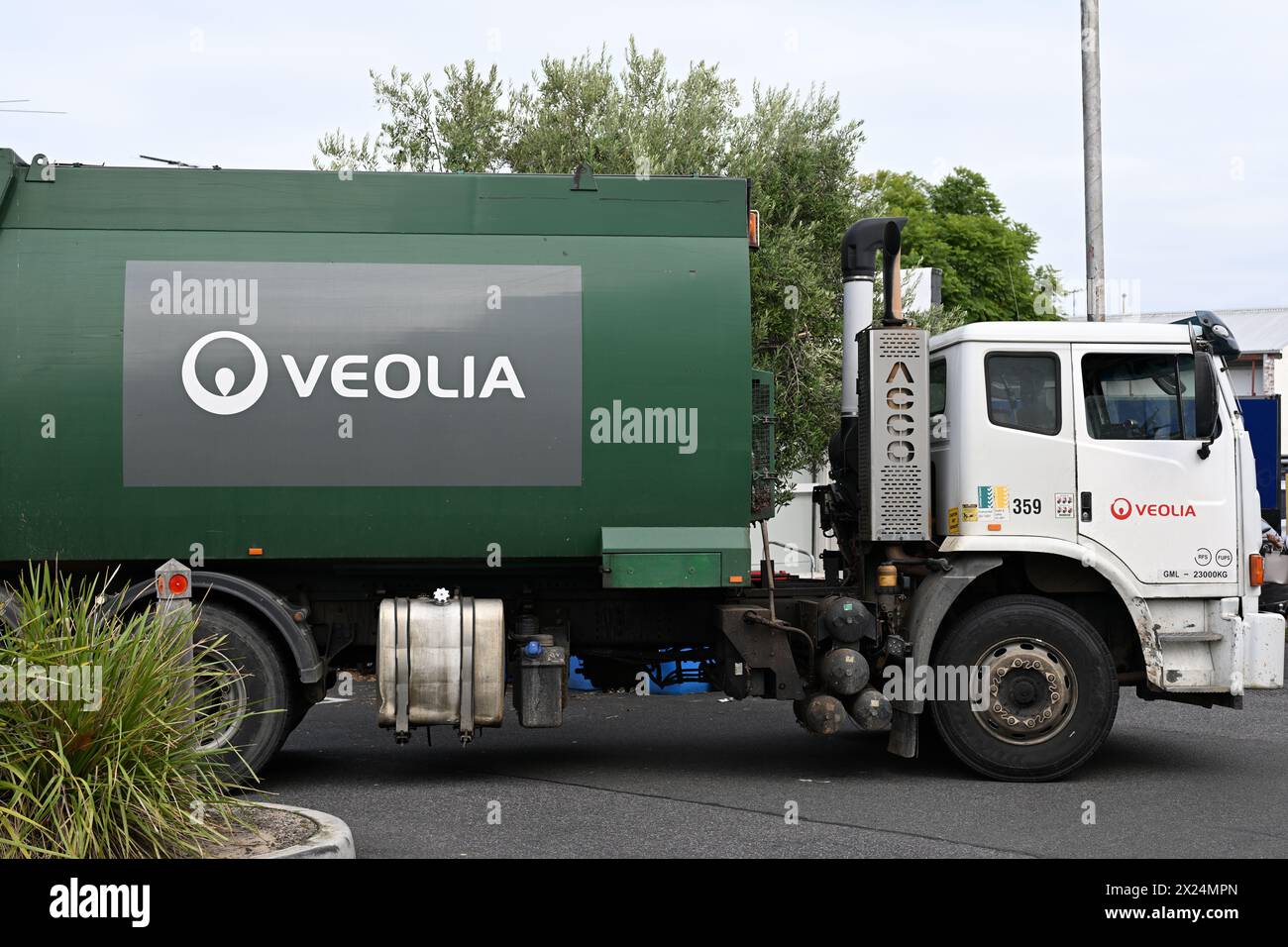 Vue latérale d'un camion poubelle Veolia vert et blanc dans un petit parking, lors d'une journée couverte Banque D'Images