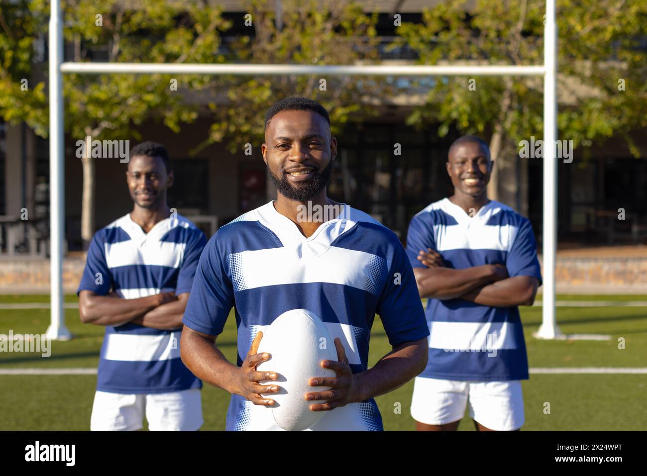 Trois jeunes athlètes afro-américains tenant un ballon de rugby, debout sur le terrain à l'extérieur Banque D'Images