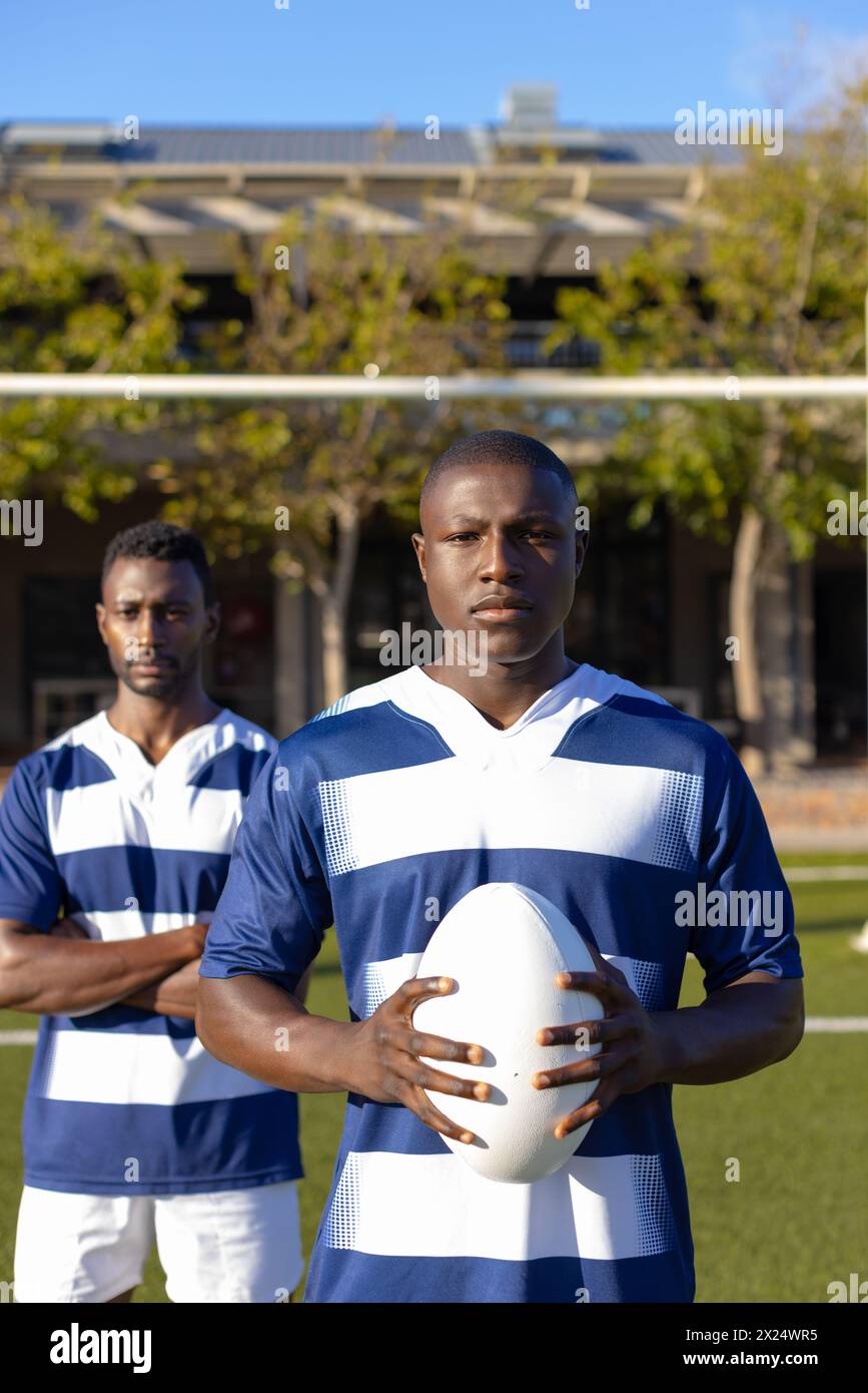 Deux jeunes athlètes afro-américains, tenant un ballon de rugby, debout sur le terrain à l'extérieur Banque D'Images