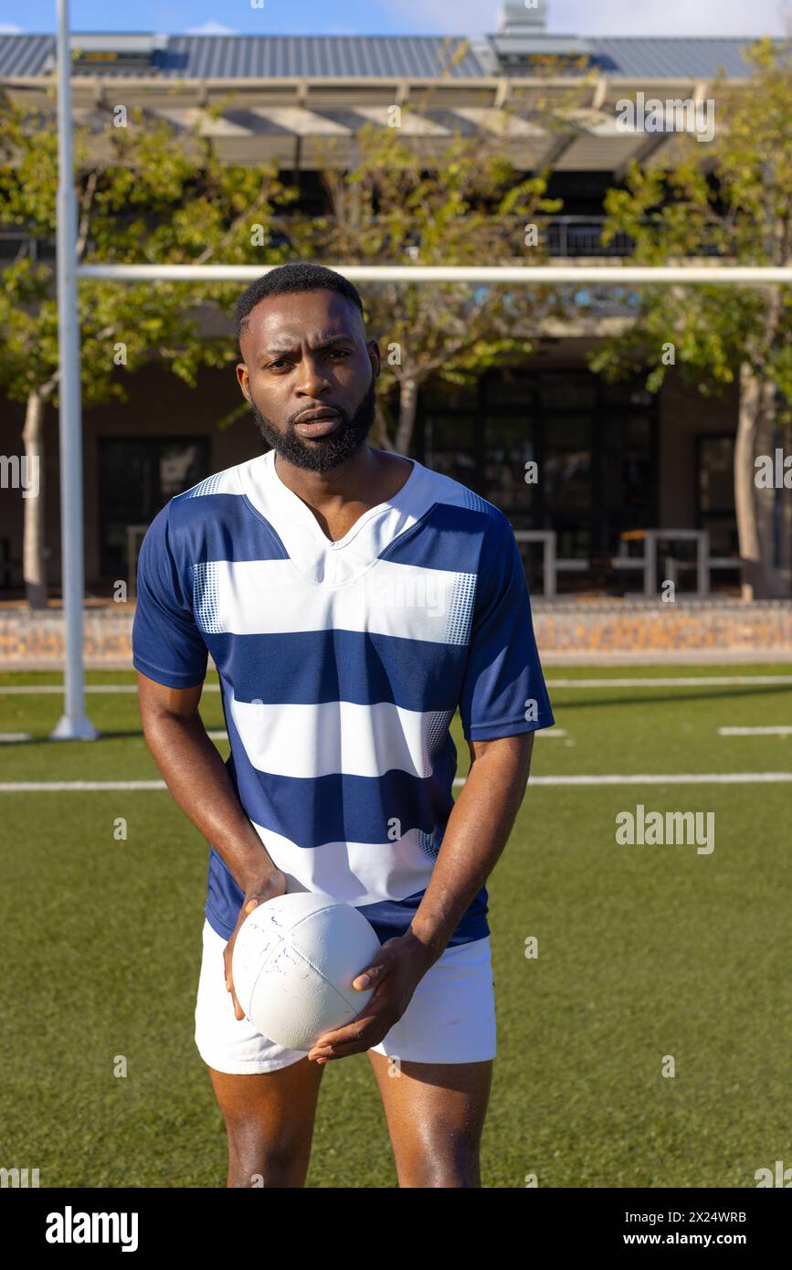 Jeune athlète afro-américain tenant un ballon de rugby sur le terrain à l'extérieur, à l'air sérieux Banque D'Images