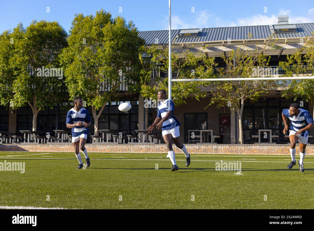 Trois jeunes athlètes afro-américains en tenue bleue et blanche jouent au rugby sur le terrain en extérieur Banque D'Images