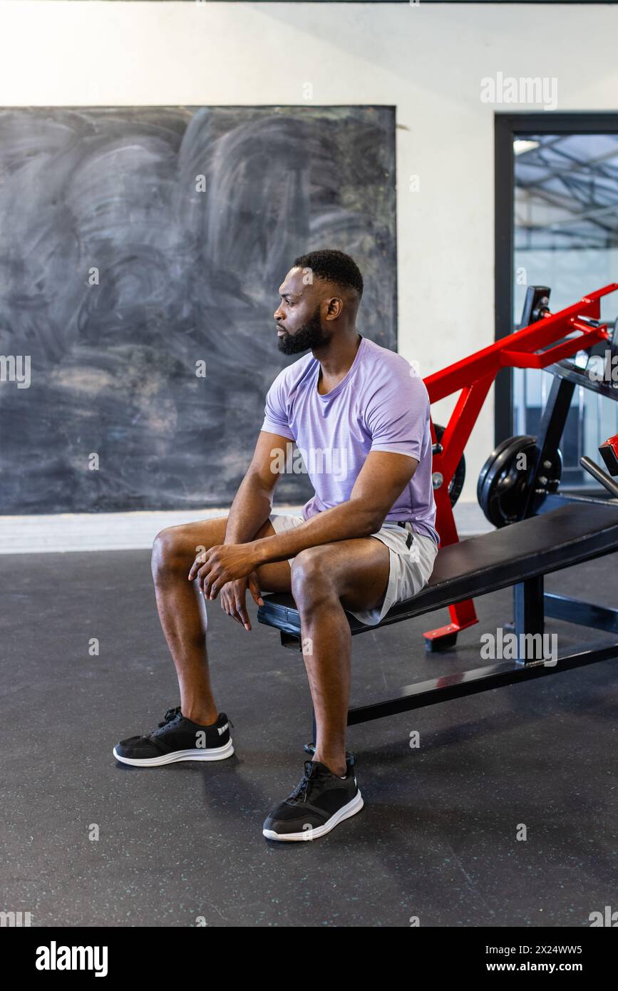 Jeune athlète afro-américain assis sur un banc dans une salle de gym, se reposant, espace de copie Banque D'Images