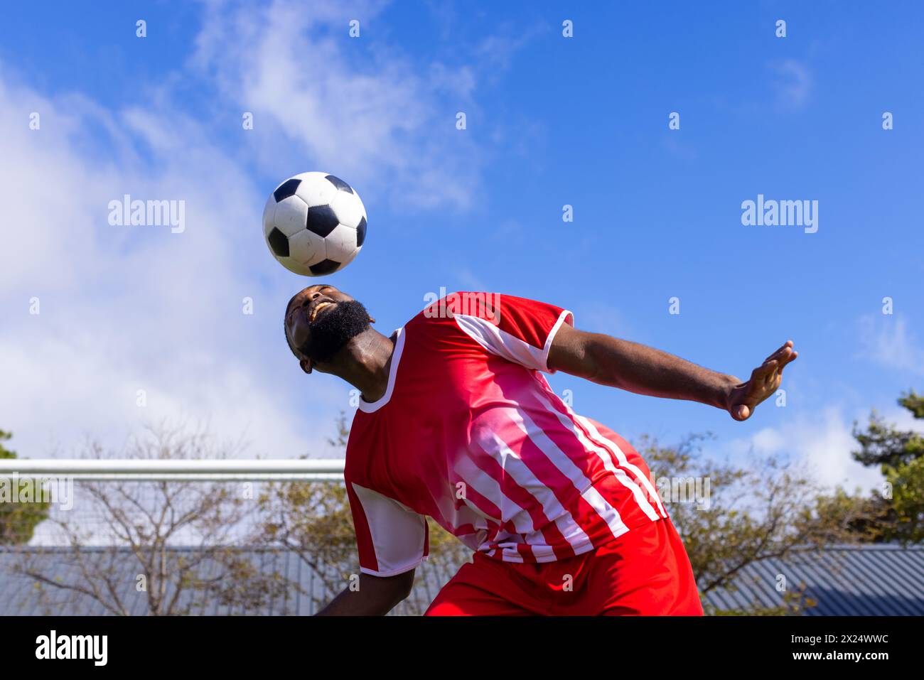 Athlète masculin noir dans la chemise rayée têtes de ballon de football à l'extérieur Banque D'Images
