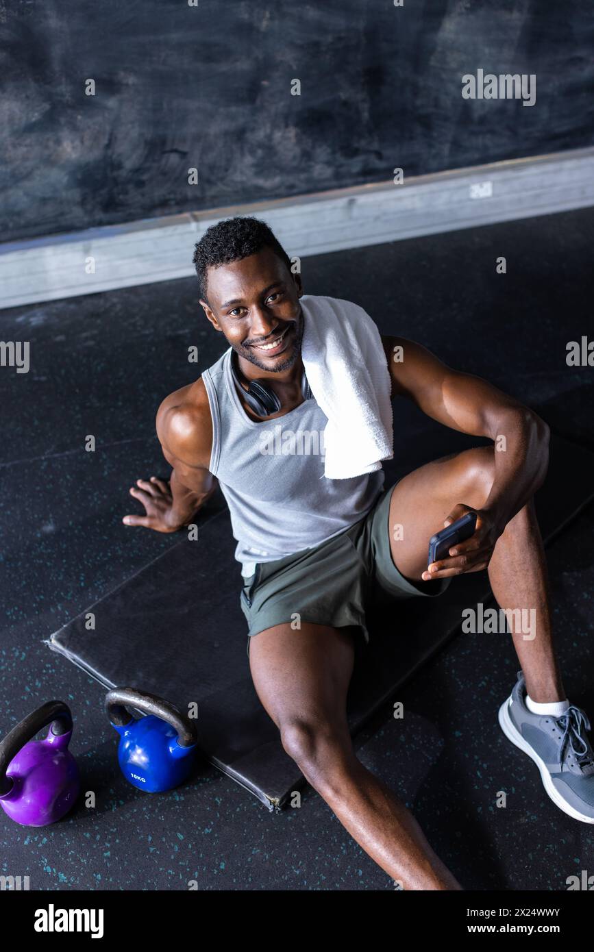 Jeune athlète masculin noir et modèle de fitness dans la salle de gym avec smartphone, au repos Banque D'Images