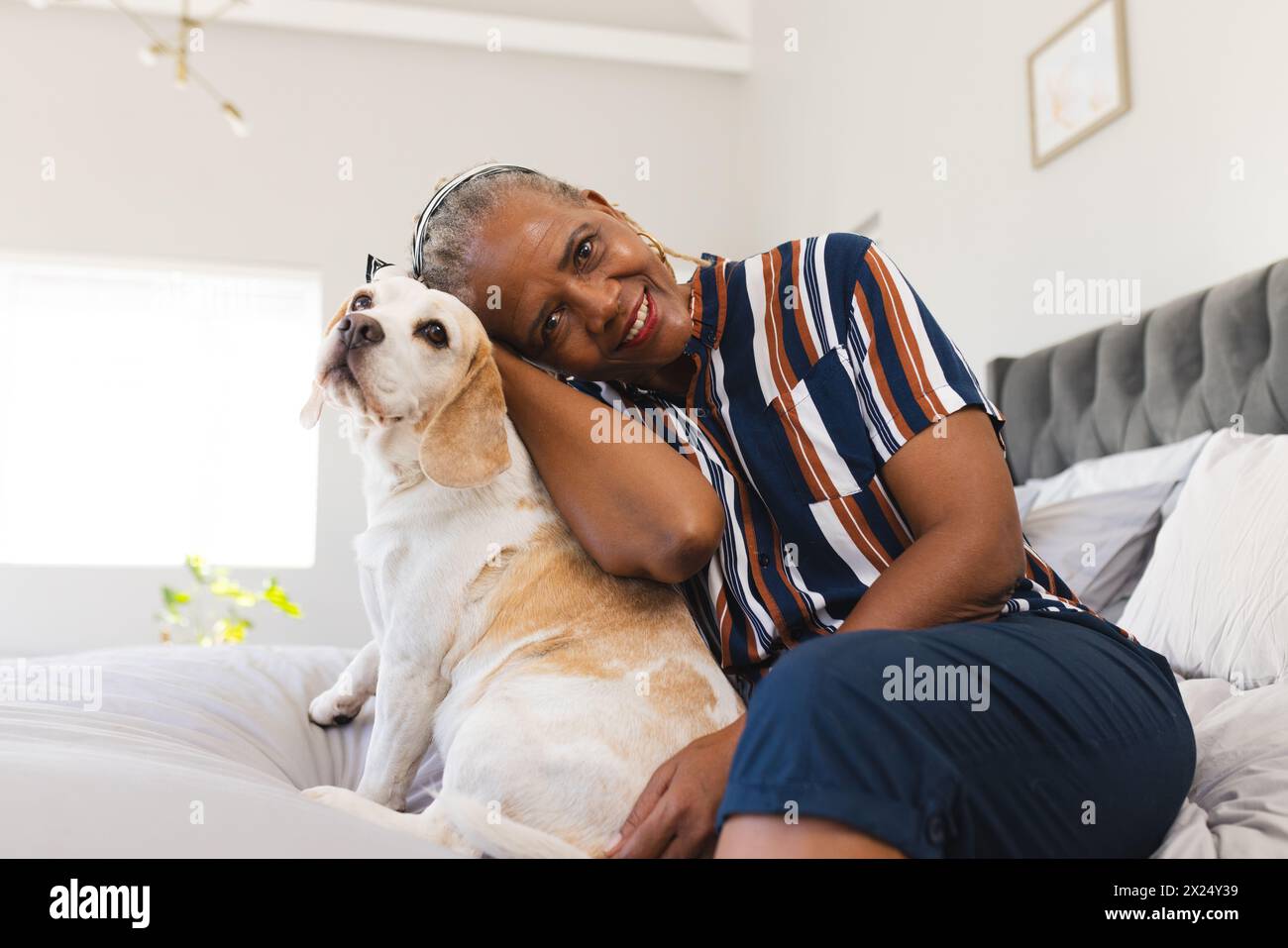Femme aînée afro-américaine assise avec son chien à la maison, les deux regardant content Banque D'Images