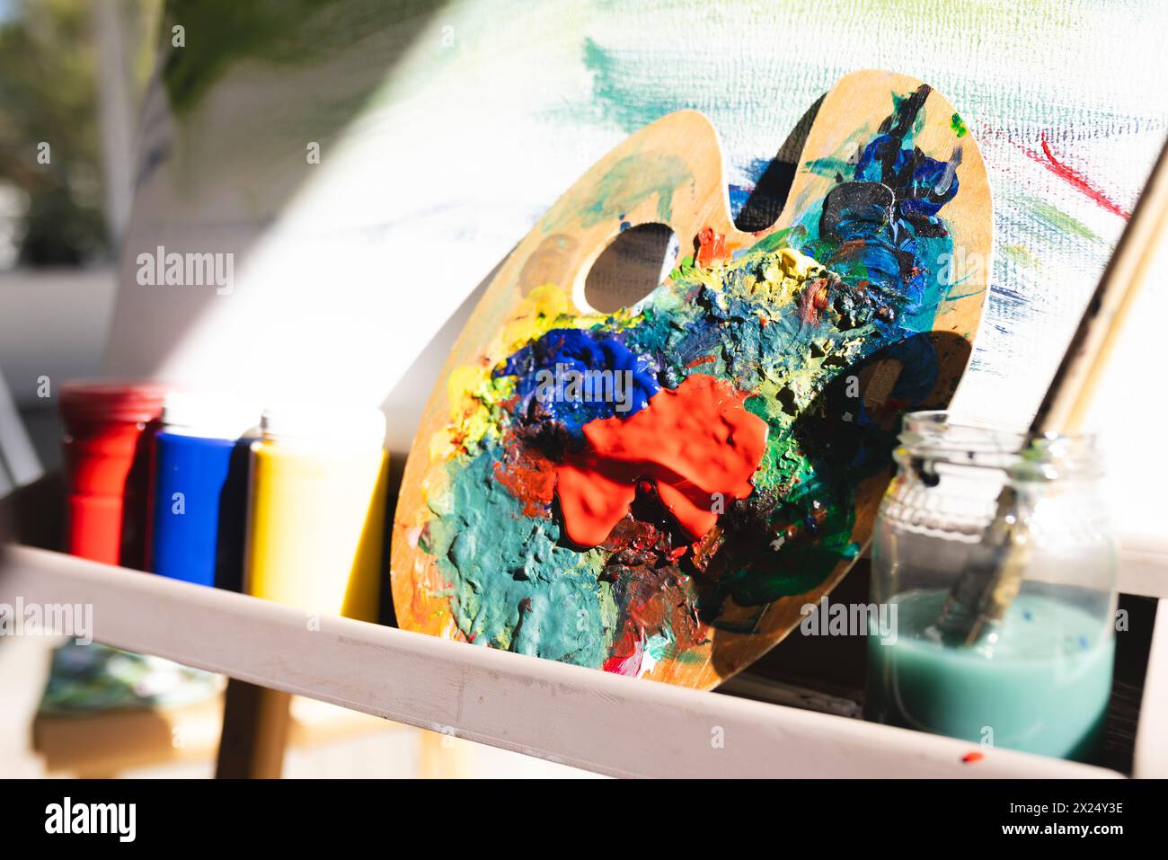 Une palette recouverte de peinture colorée repose sur un chevalet à la maison. La lumière du soleil brille sur les toiles, mettant en évidence des teintes vibrantes, inaltérées. Banque D'Images