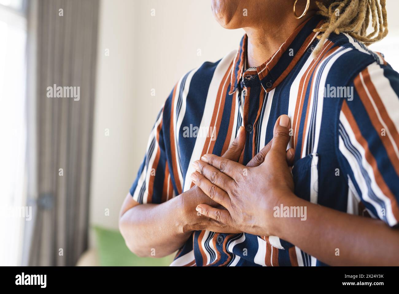 Une femme afro-américaine senior avec les mains sur sa poitrine se tient à l'intérieur à la maison, espace de copie Banque D'Images