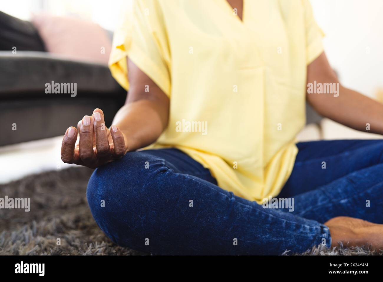 Femme aînée afro-américaine assise les jambes croisées à la maison, pratiquant la méditation Banque D'Images