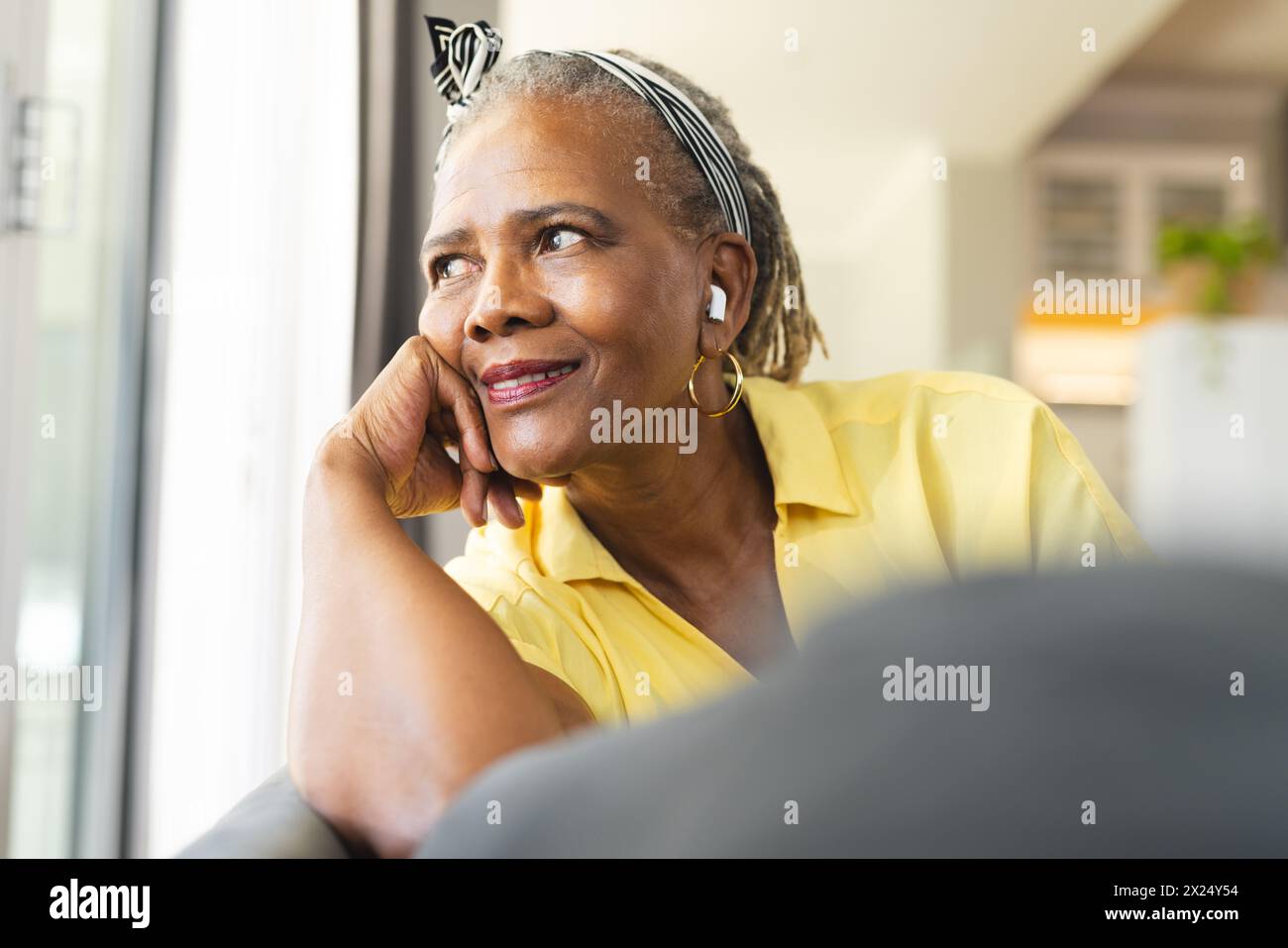Une femme afro-américaine senior regardant par la fenêtre à la maison, pensant Banque D'Images