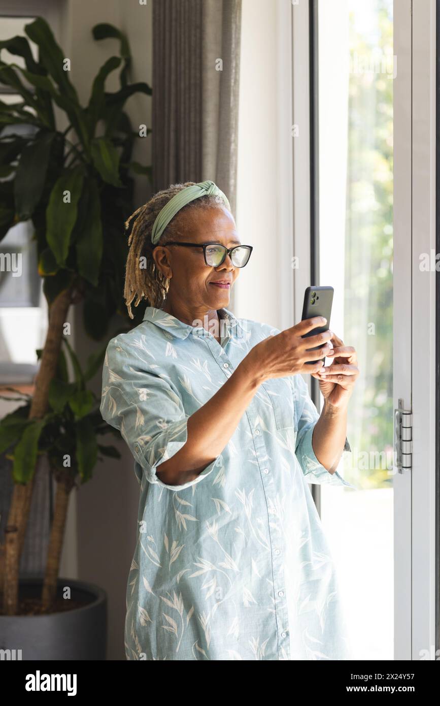 Une femme afro-américaine senior portant des lunettes tenant un smartphone à la maison Banque D'Images