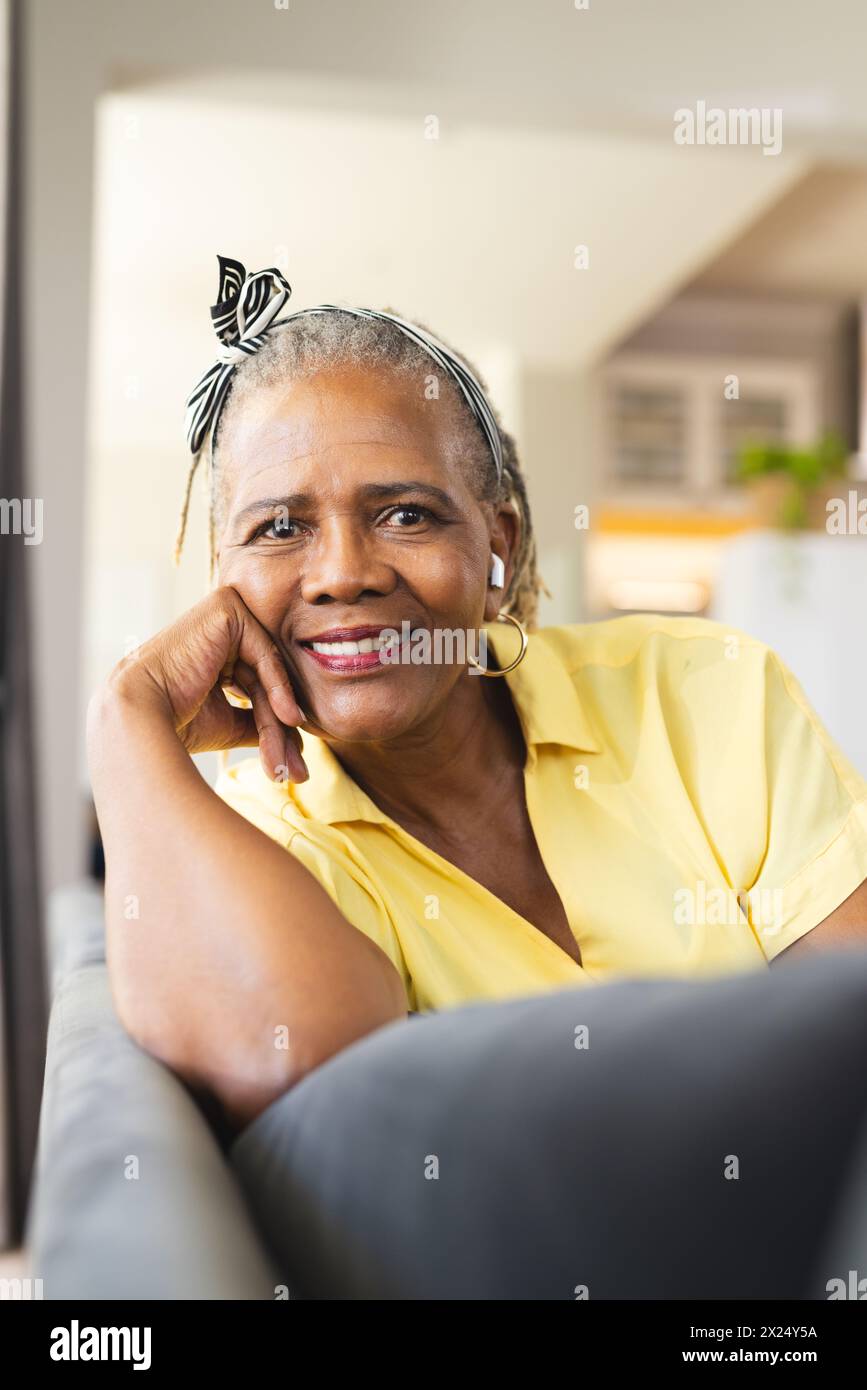 Une femme afro-américaine senior avec un sourire chaleureux assise sur un canapé à la maison Banque D'Images