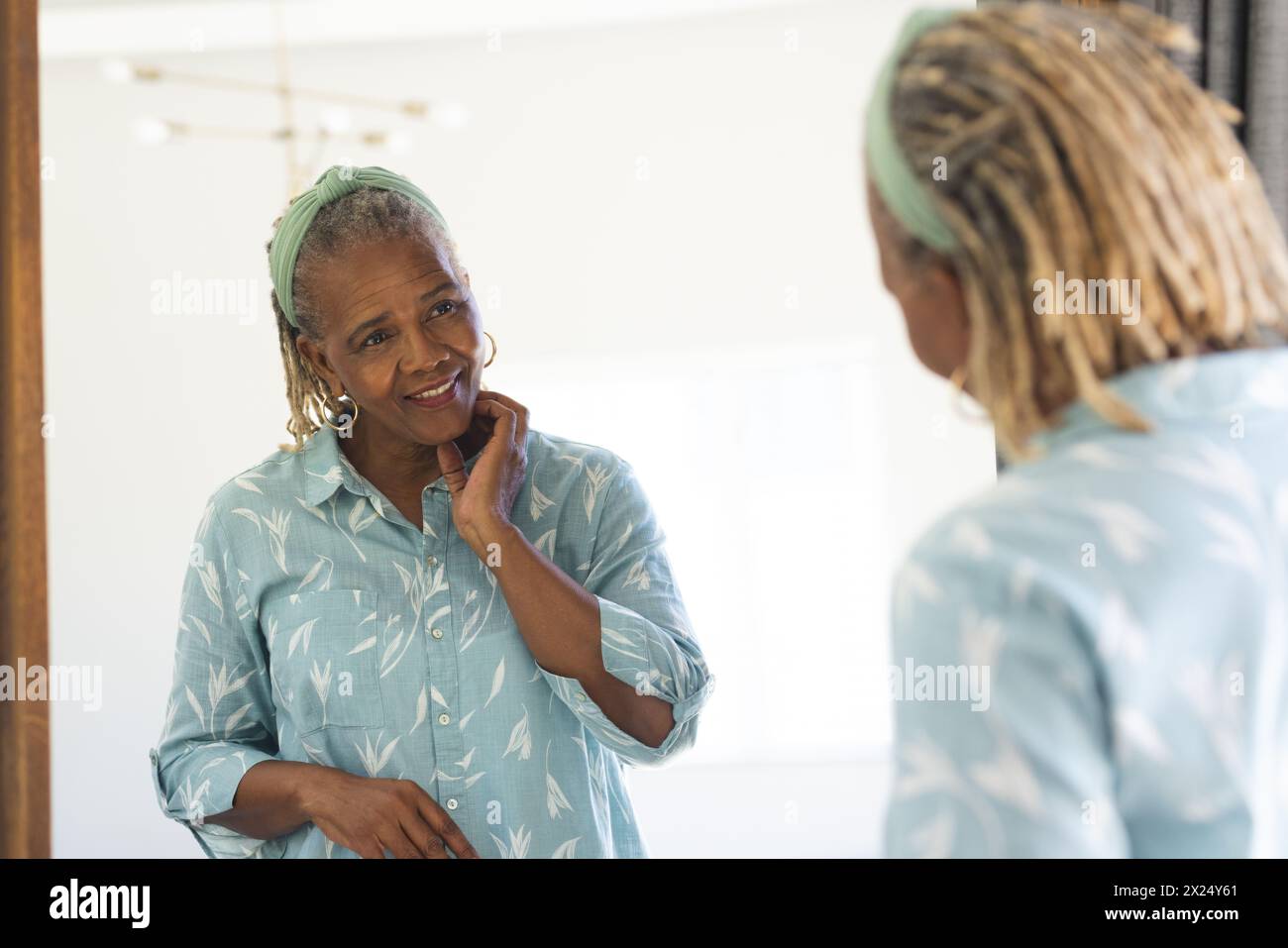 Une femme afro-américaine âgée aux cheveux gris regarde un miroir à la maison Banque D'Images