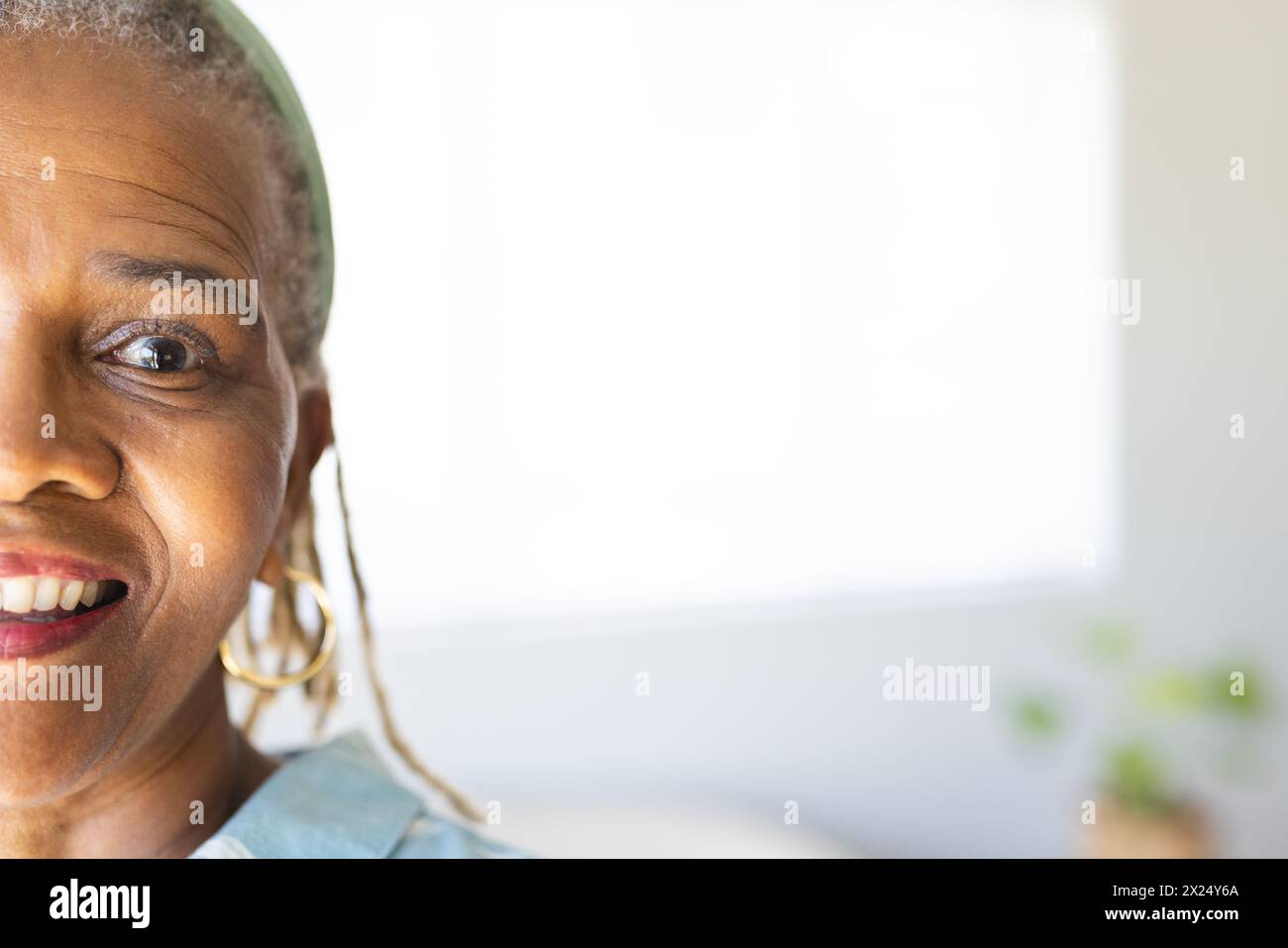 Femme aînée afro-américaine avec les cheveux gris portant des boucles d'oreilles est souriante à la maison, espace de copie Banque D'Images