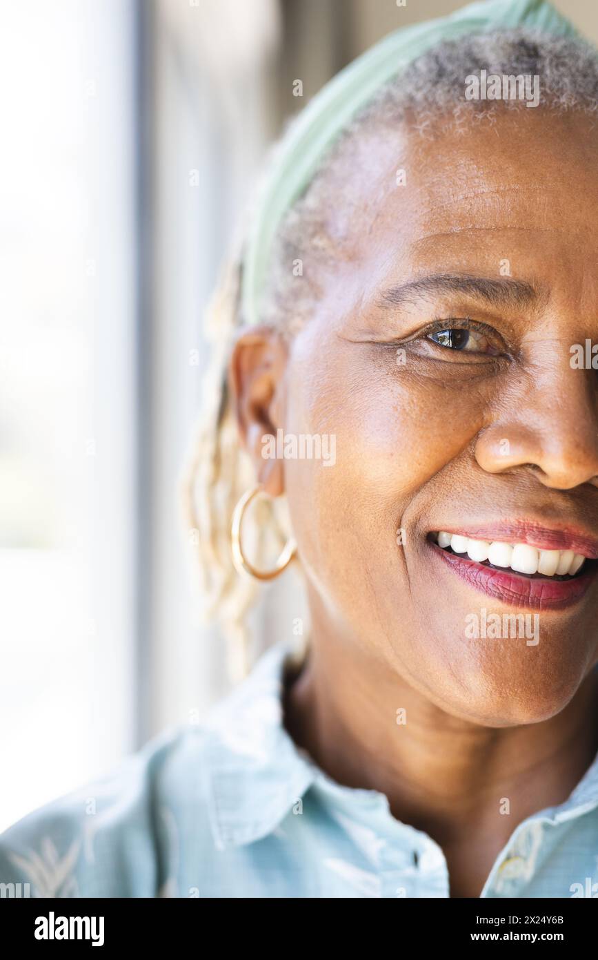 Femme aînée afro-américaine portant des boucles d'oreilles cerceau est souriante à la maison, copiez l'espace Banque D'Images