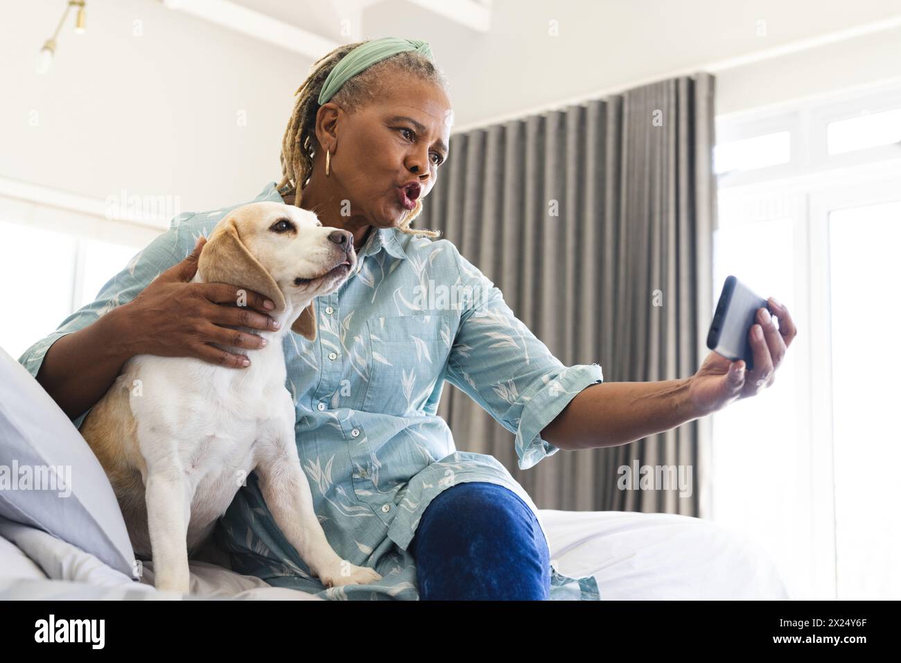 Femme aînée afro-américaine assise avec un chien à la maison, prenant selfie, tenant un smartphone Banque D'Images