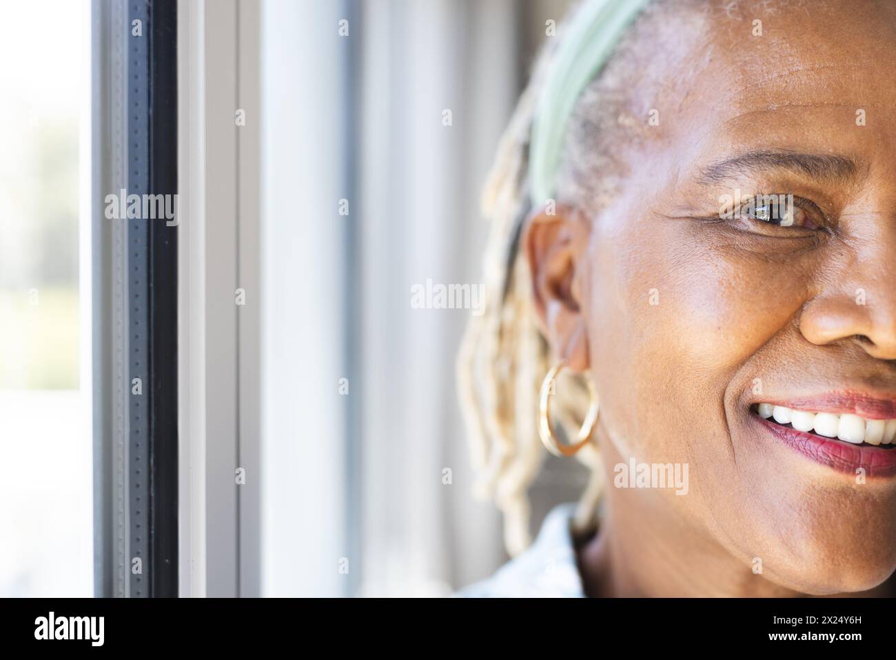 Une femme afro-américaine senior avec un sourire brillant debout près d'une fenêtre à la maison, espace de copie Banque D'Images