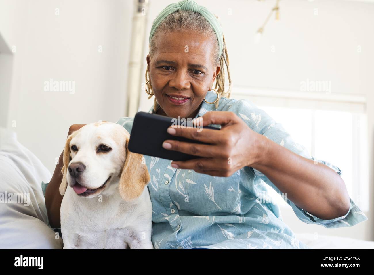 Femme aînée afro-américaine tenant un smartphone, prenant selfie avec un chien à la maison Banque D'Images