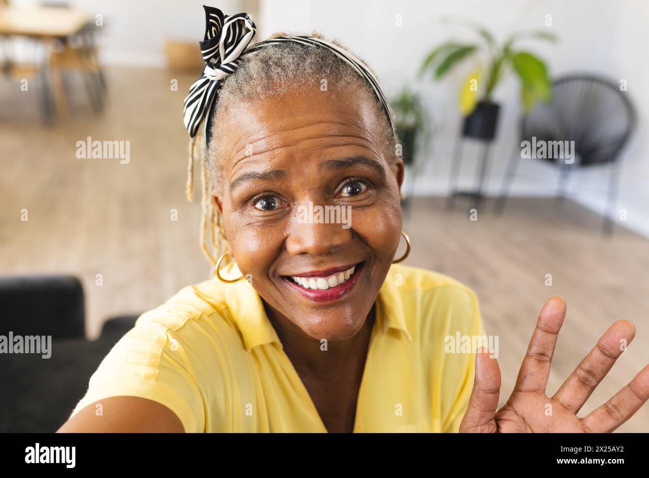 Femme senior noire en chemise jaune donne signe de paix sur appel vidéo à la maison Banque D'Images