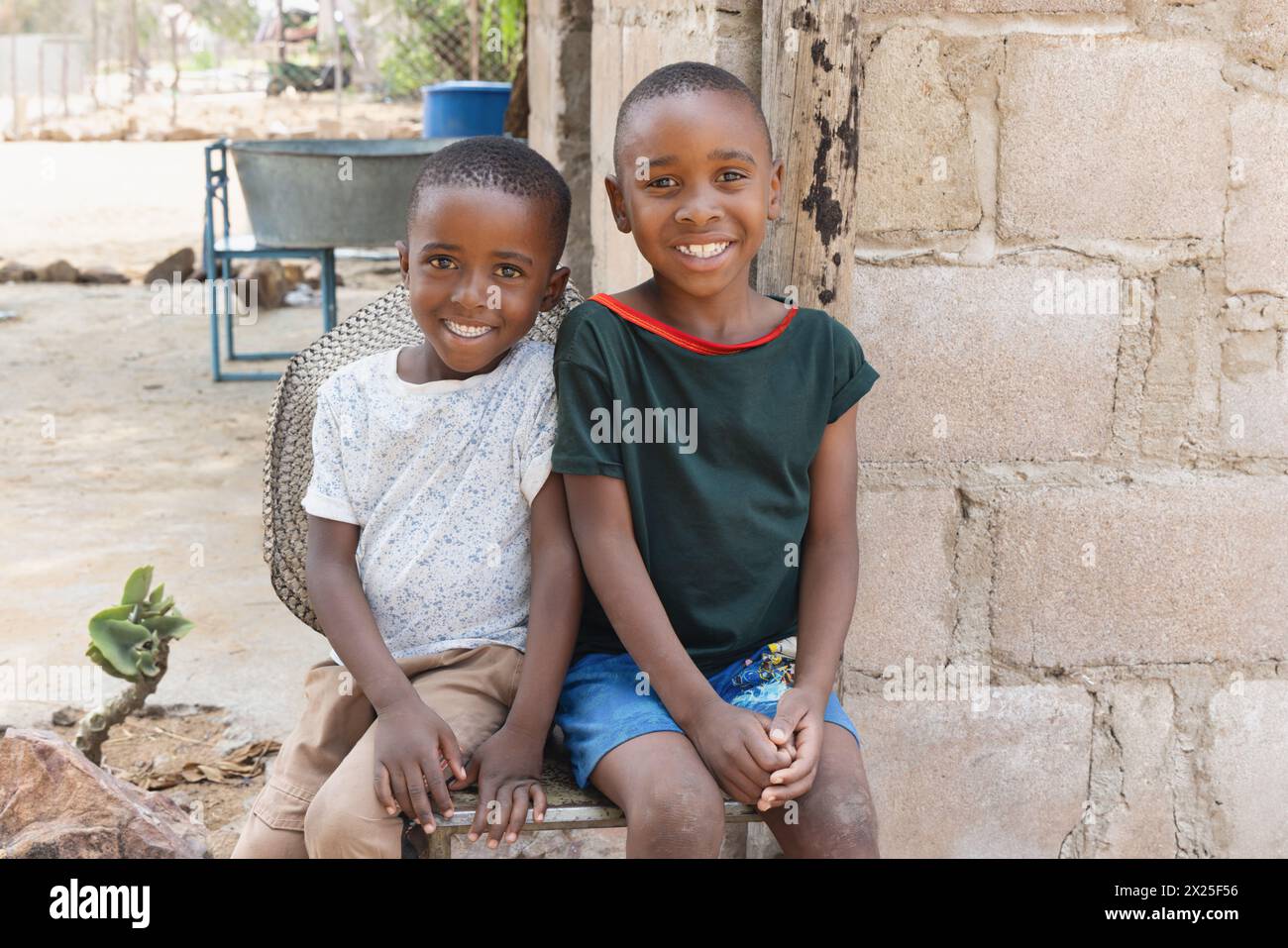 village deux enfants africains, assis sur une chaise dans la cour, habillés décontractés Banque D'Images