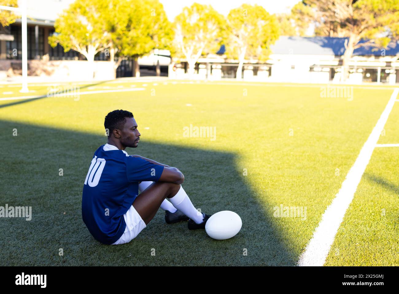 Jeune athlète afro-américain assis sur un terrain de rugby, regardant réfléchi, espace de copie Banque D'Images
