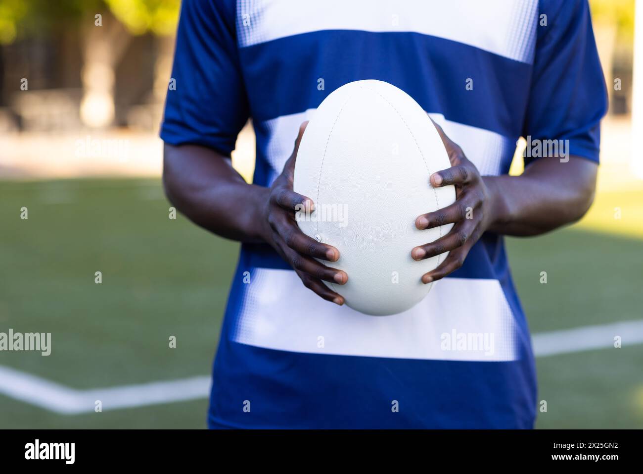 Jeune athlète masculin noir avec ballon de rugby en maillot bleu et blanc sur le terrain Banque D'Images