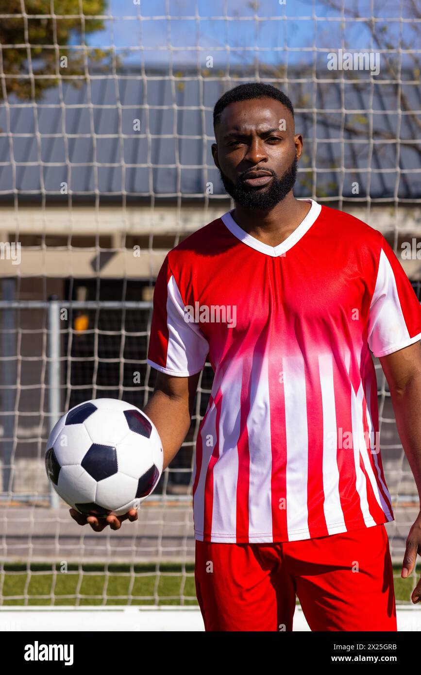 Athlète masculin noir avec ballon de football se tient par filet de but Banque D'Images